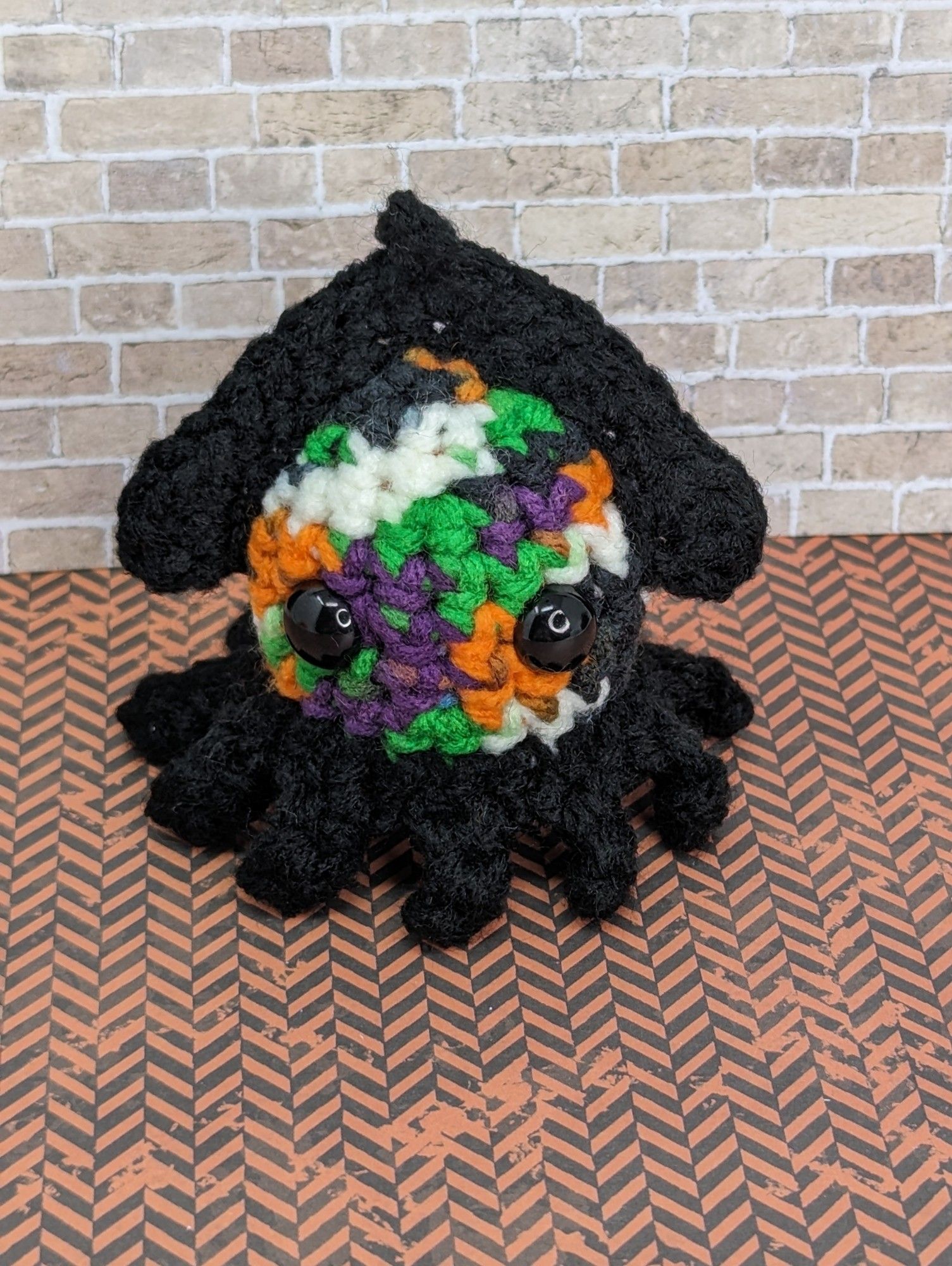 A multicolored crocheted squid: it's Halloween themed, in green, purple, orange, white, and black