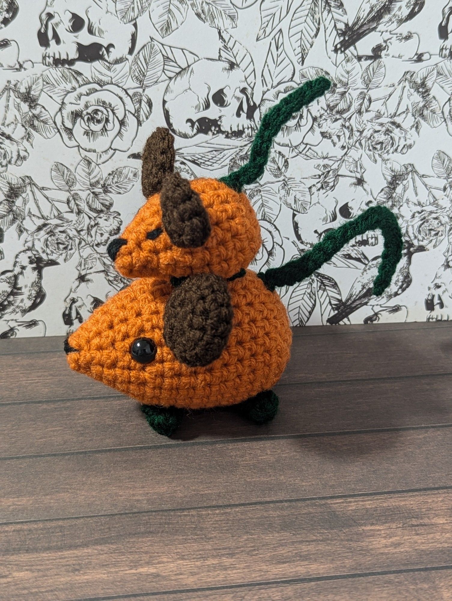 Two crocheted mice, both dressed up as pumpkins; one of them is tiny and is perched on top of the larger one