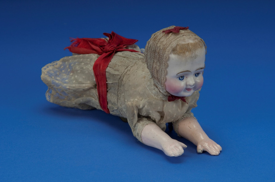 A crawling baby doll, with a slightly less horrifying face then the prototype, and clothed, which hides the machinery inside. The doll now wears a bonnet and dress, which were white, but are now distinctly Miss Havisham, and there is a large red ribbon round her midriff