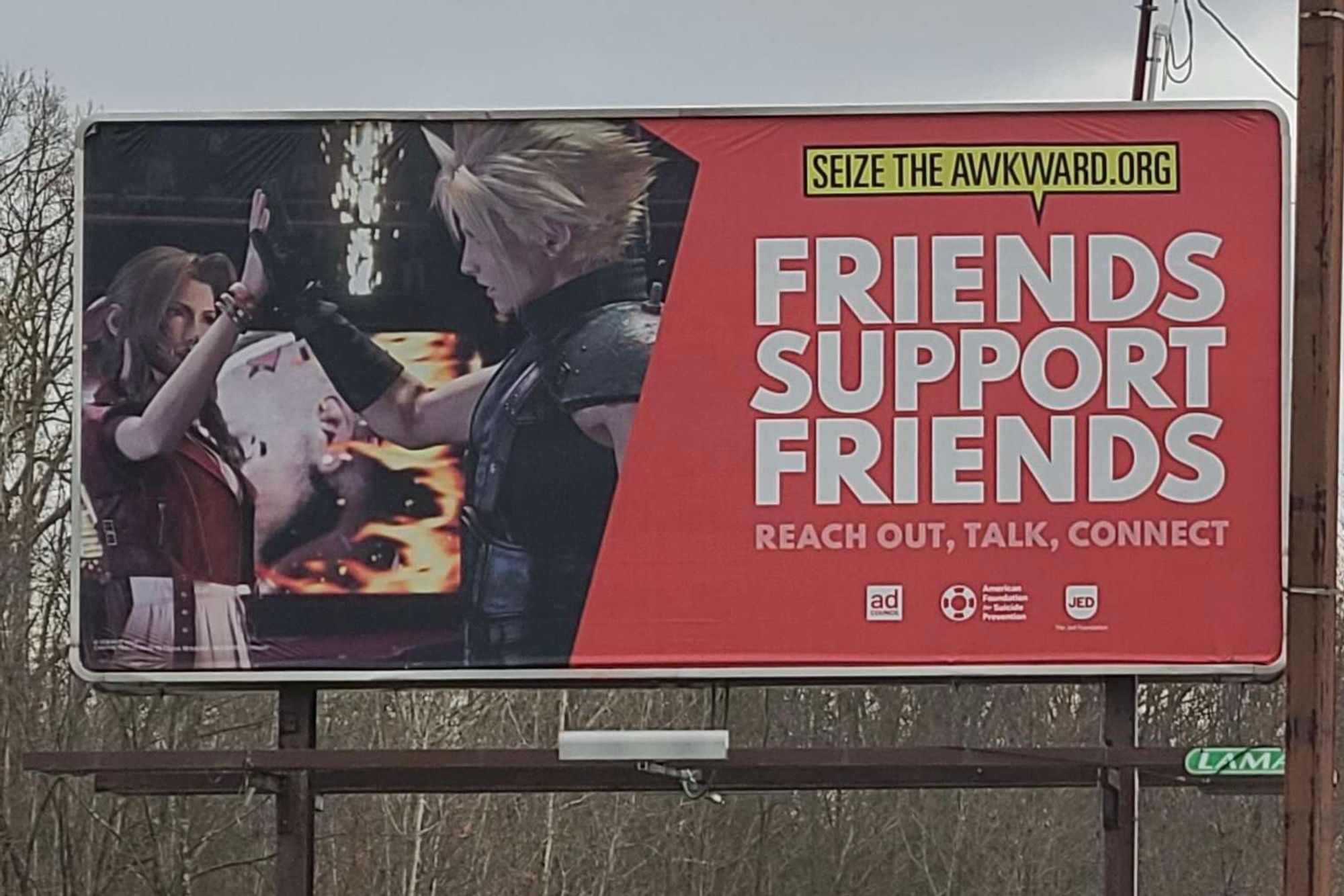 A photo of a billboard. The right half reads SEIZETHEAWKWARD.ORG / FRIENDS SUPPORT FRIENDS / REACH OUT, TALK, CONNECT, with logos for the Ad Council, American Foundation for Suicide Prevention, and The Jed Foundation. On the left half is an image of Cloud and Aerith from Final Fantasy VII Rebirth high-fiving.