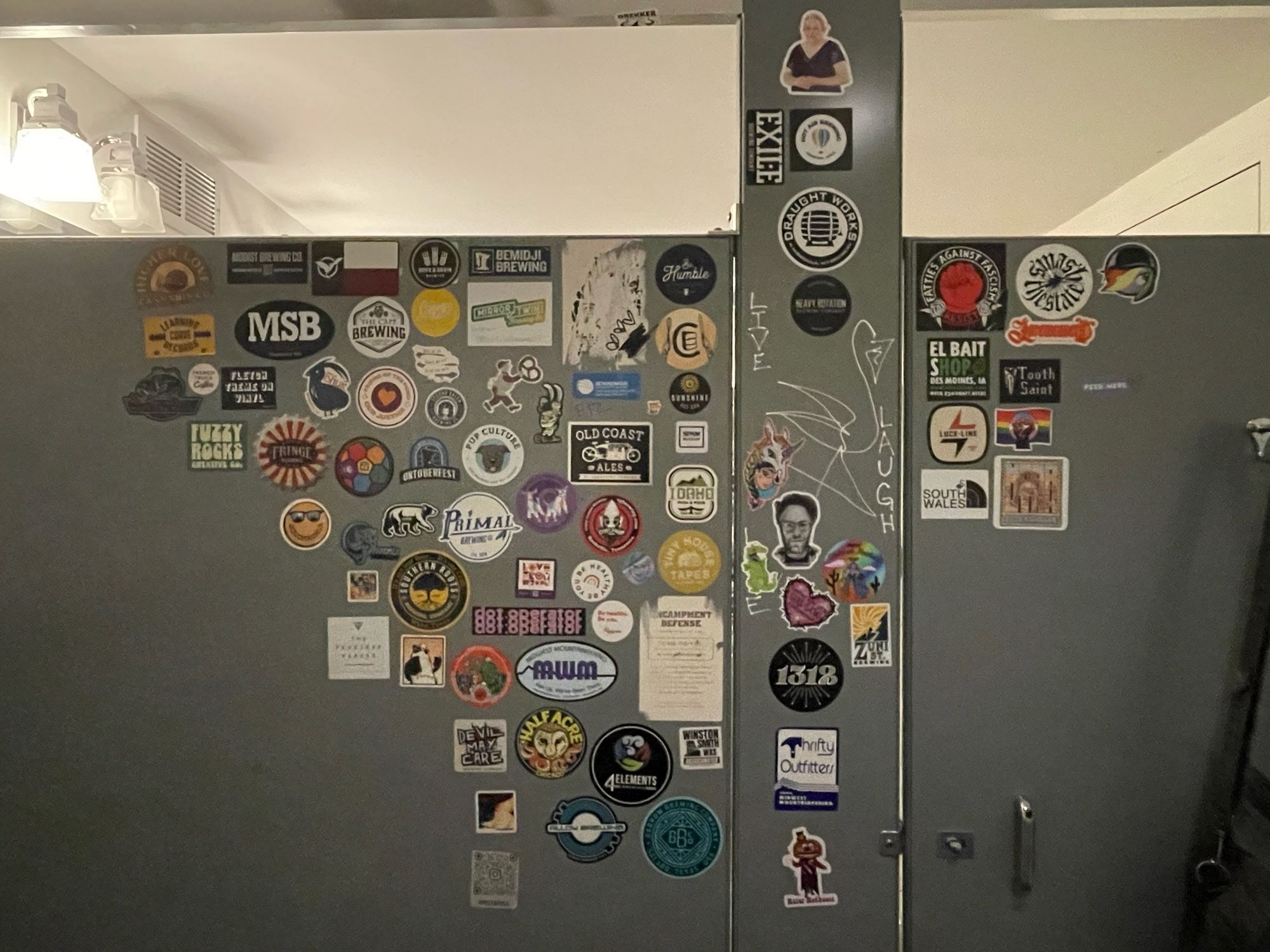 A lot of stickers inside a bathroom stall, mostly advertising breweries or Minnesota nonprofit organizations, close together in a sort of orderly way