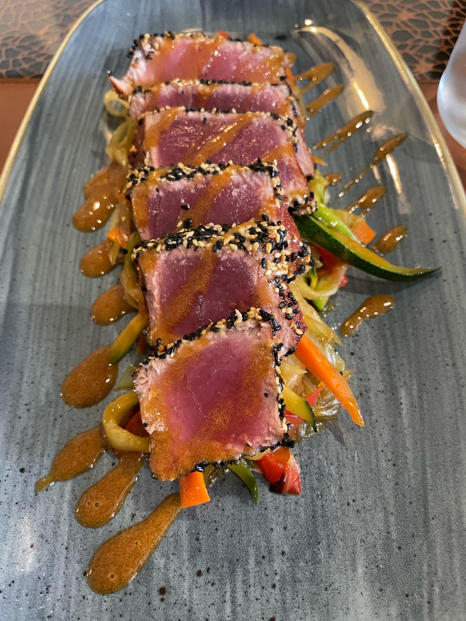 Slices of seared sesame crusted tuna on a bed of julienned vegetables with sauce