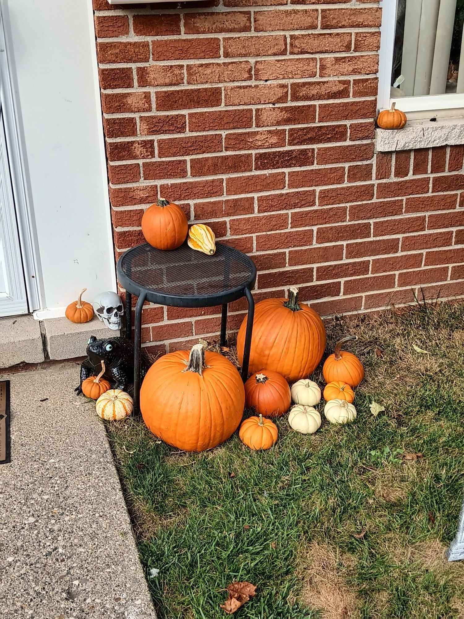 Outside of a red brick house with many pumpkins. Somewhere a cat is lurking.