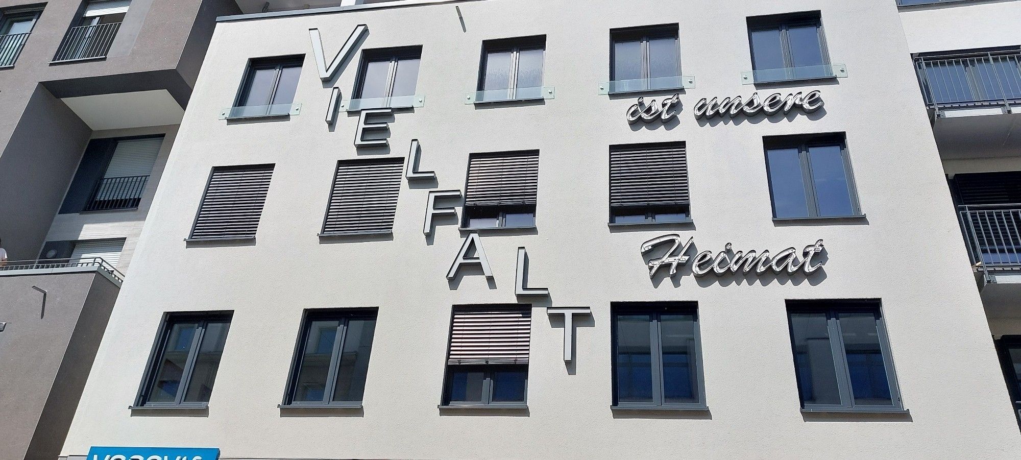 Bildbeschreibung
Gebäudefassde in Essen-Rüttenscheid. 3 Etagen mit je 5 Fenstern zur Straße. Auf der hellen Fassade steht in Großbuchstaben "VIELFALT" leicht
versetzt in einer Diagonalen und daneben steht in Schreibschrift "ist unsere Heimat". Bild aus dem Demozug "Gegen den
Afd-Parteitag".