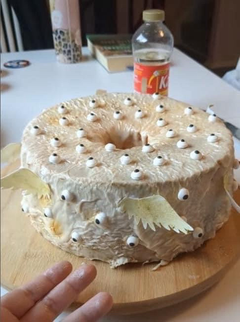 Image of a golden frosted cake with pale yellow wings attached to the sides & a fuck ton of tiny eyeballs