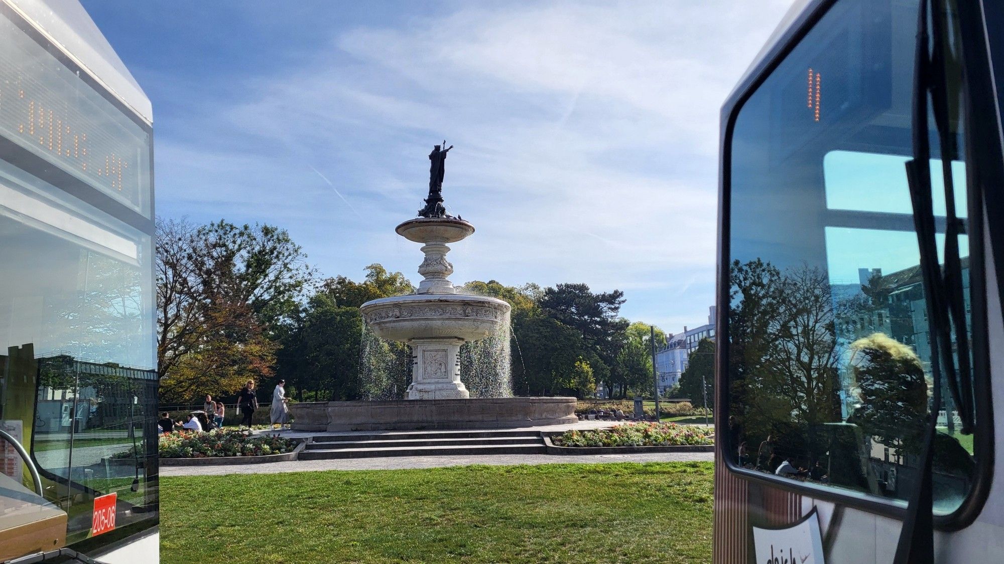 Blick zwischen zwei Trams auf einen Springbrunnen