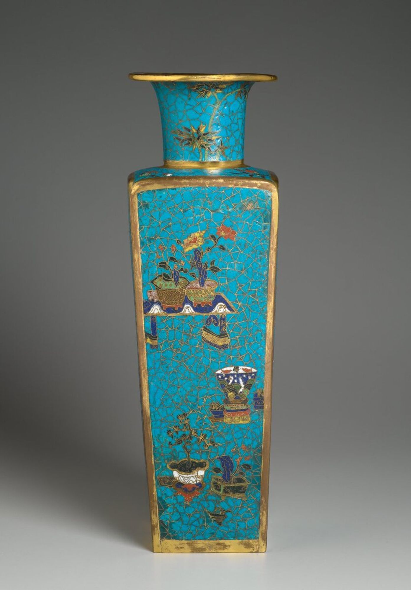 The shape of this vase was popular during the Ming and Qing dynasties and possibly modeled after European bottle of the period. The cracked ice background decoration draws its inspiration from a ceramic technique initiated during the Kangxi era. The four sides of the vase depict plants, rocks, vases, bronze vessels, books, scrolls, a "qin," a sword and a fan in the shape of a banana leaf -- objects which signify the comfortable everyday life of the urban scholar-official. This type of composition, with objects floating freely, is also seen in eighteenth century ceramics, lacquerware and furniture decoration. It was an icon of eighteenth century China and may well be a reflection of the prevailing materialistic urban culture. The use of cloisonné for scholarly objects at this time also indicates a change of attitude brought about by the imperial patronage. Soon after its introduction to China, cloisonné was criticized by an early Ming Confucian scholar. Cao Zhao opposed the rich decoration of cloisonné, which presented a striking contrast to the monochrome ink paintings favored by the literati from the Yuan time onwards. Undoubtedly, the cloisonné was very popular with the ladies of the imperial court, and their patronage and taste may have influenced production. In deep cobalt blue, red, yellow, dark green, light green, brown, and white on a very deep turquoise background.