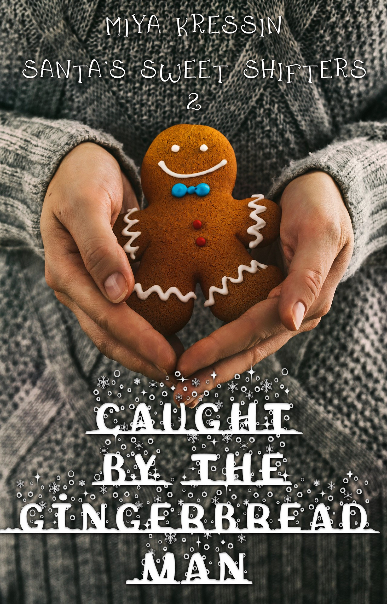 photo of a book cover of a close up of a grey cabled sweater  with a gingerbread cookie cradled carefully in two hands.. snowflake decorated white text across the bottom reads "Caught by the gingerbread Man" while white text at the top reads "Santa's Sweet Shifters 2" with the author name of "Miya Kressin"