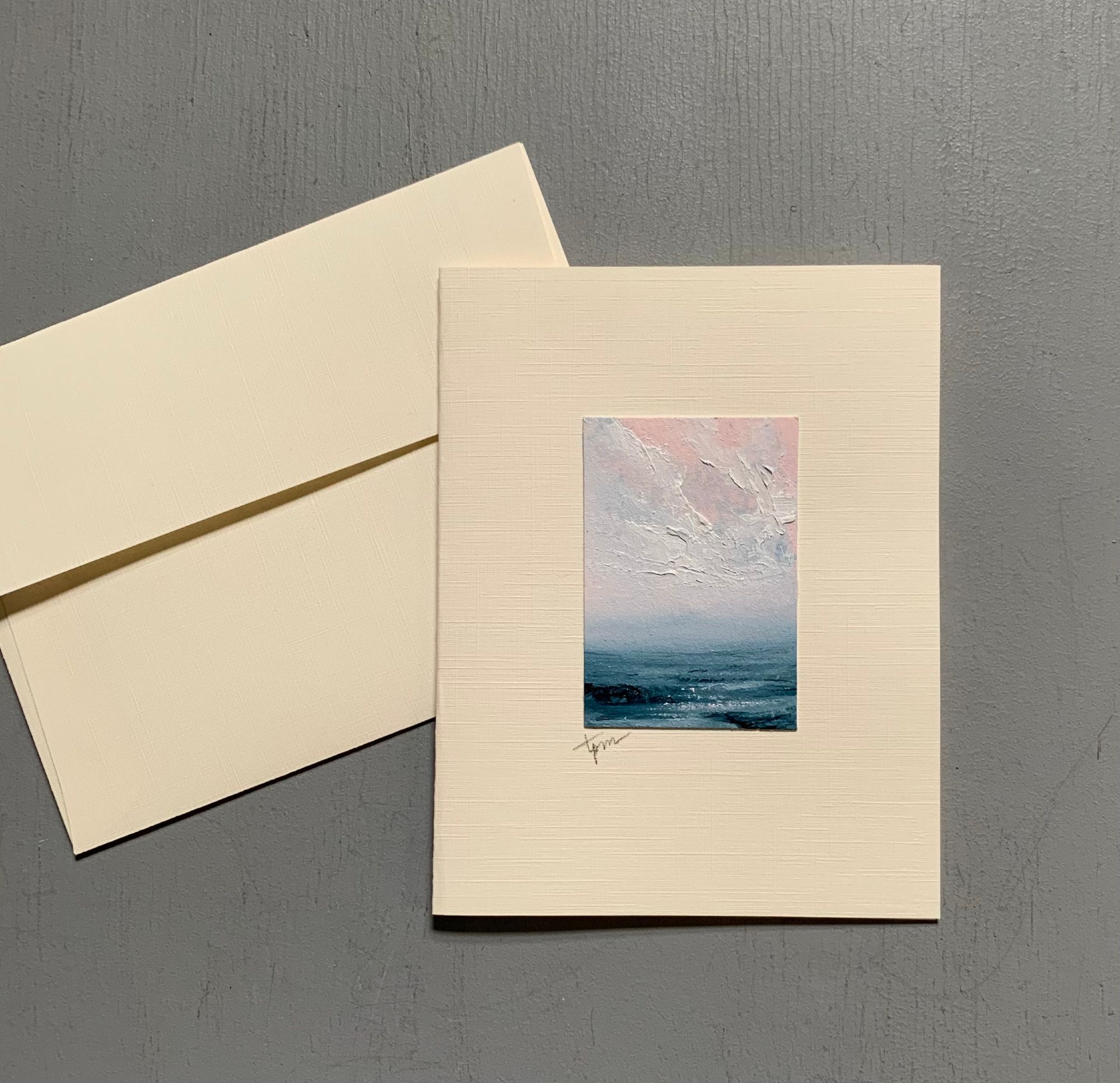 Photo of Fine Art Card No. 2414 by Tisha Mark, pictured here with a matching envelope. The seascape is vertically oriented and is a seascape with textured cloud formations in a pink-toned sky over a deep blue sea with a rocky coast.