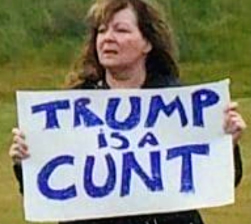 The late Janey Godley holding a sign that says "Trump is a cunt".