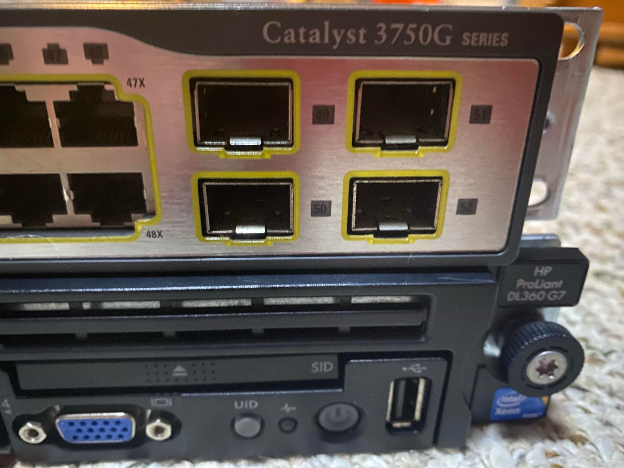 Close-up of the end of the two boxes from the previous picture.  The top is labelled “Catalyst 3750G series” and has 4 SFP ports.  The bottom is labelled HP ProLiant DL360 G7 and features some small buttons and lights, a VGA port, and a USB port.