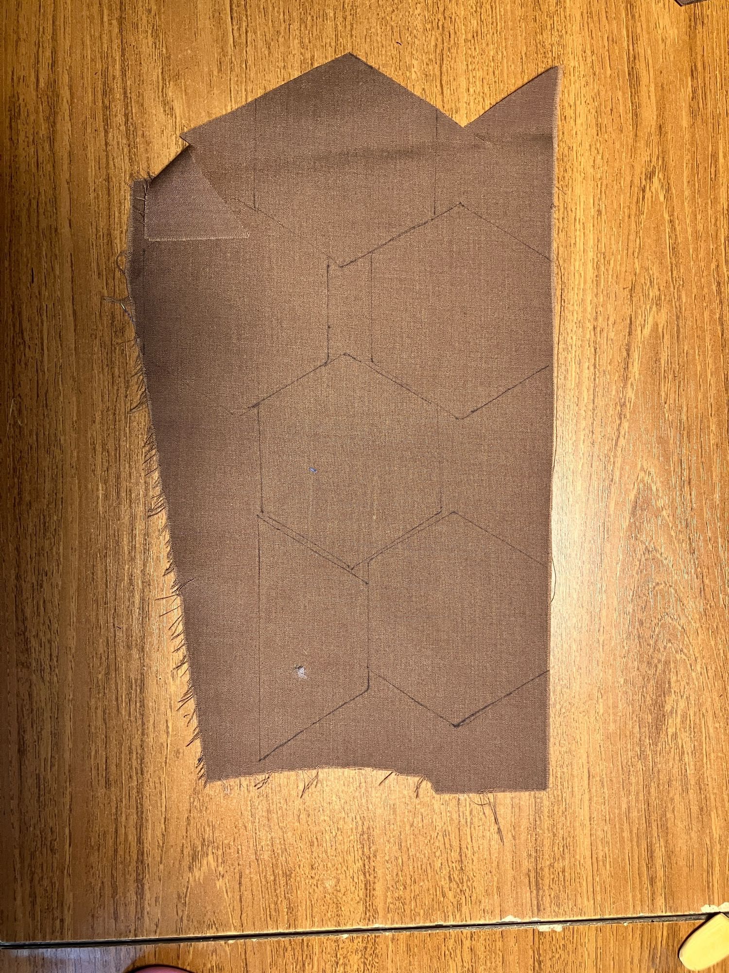 A piece of brown scrap fabric with five whole and one half hexagon shape marked on it. The lines are done in a fine black marker.