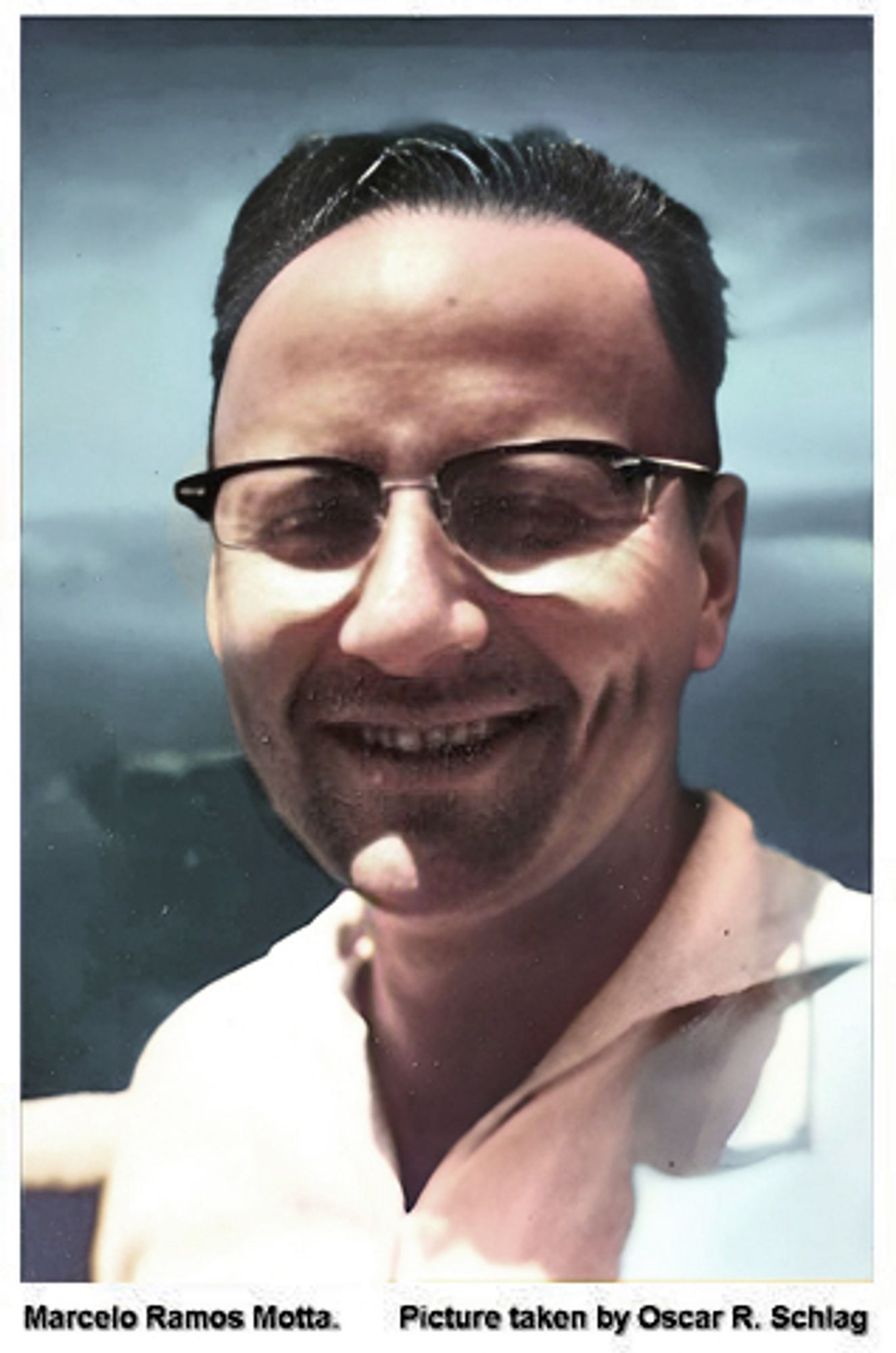 Marcelo Ramos Motta, a smiling man in a white collared shirt.  He has a prominent nose, a rounder face, and glasses with a thick black top frame.