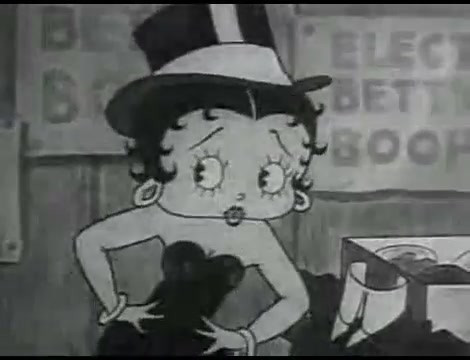 Betty is on the stage with both hands on her wrist. She is wearing a small dress, a big pair of earrings and a top hat. 