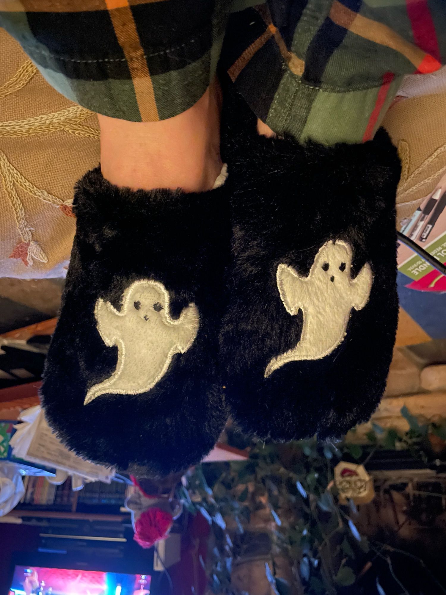 my feet contained in black furry slippers with spooky white ghosties on the top. photo flipped so the ghosts don’t look like they’re doing headstands