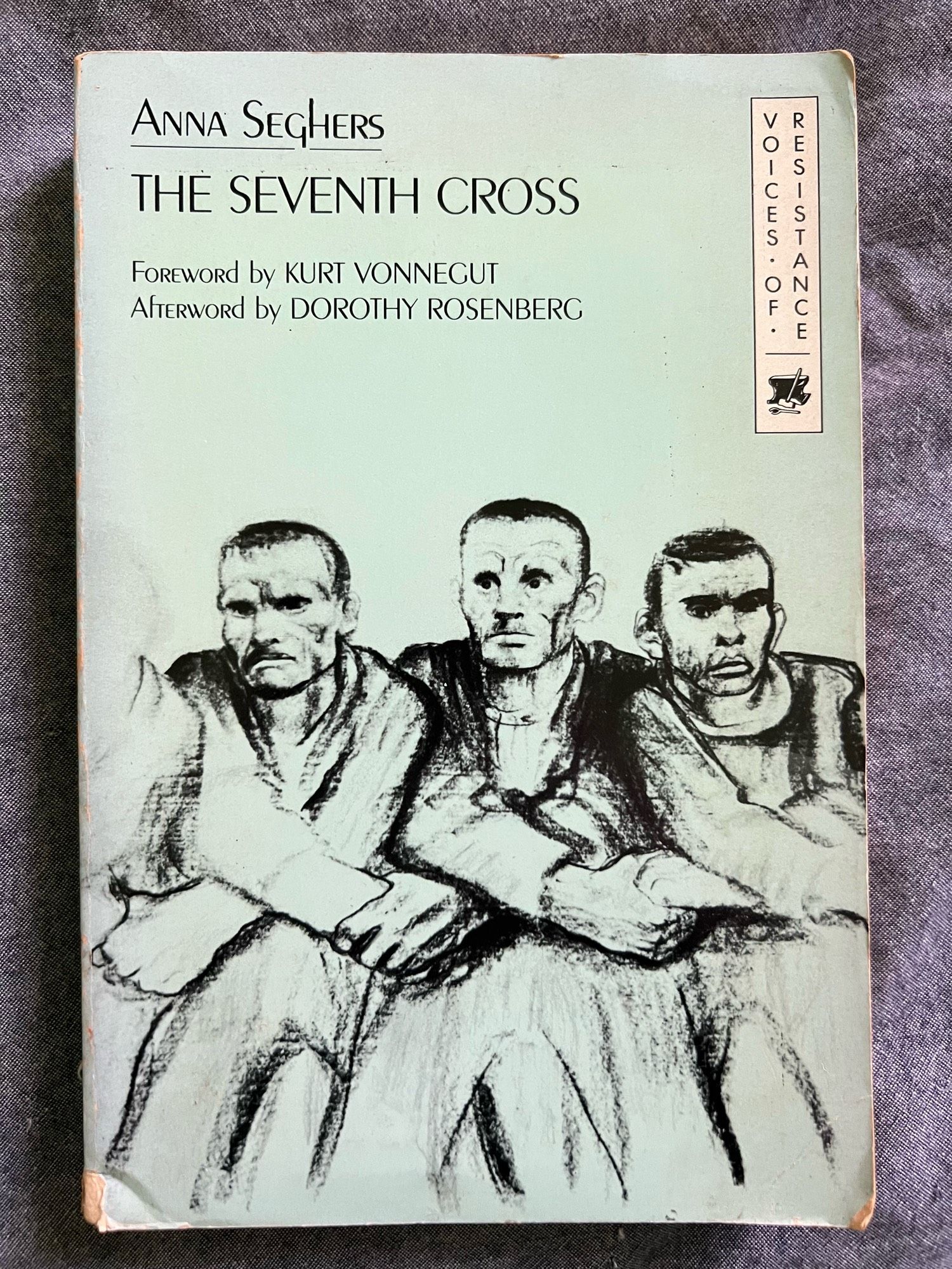 Cover of the Monthly Review Press edition of Anna Segher’s novel The Seventh Cross. Displayed on a pale green background is a detail of the lithograph Propellor Song-Solidarity by Käthe Kolwitz. It shows three men staring forward with their arms interlinked.