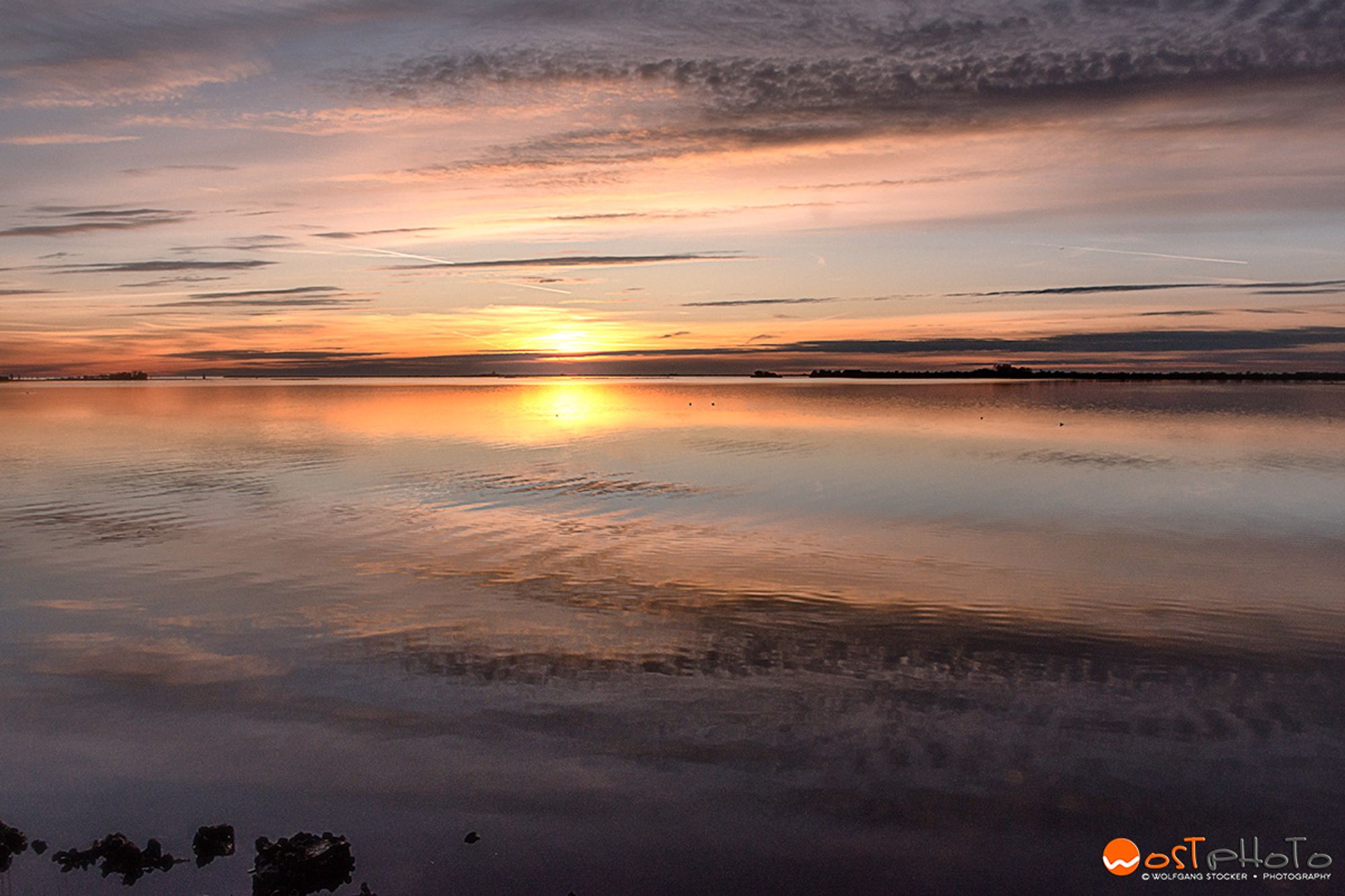 Sunset over the lagoon. Fluffy clouds in the pinkish-blue sky mirroring in the shallow water of the sea.