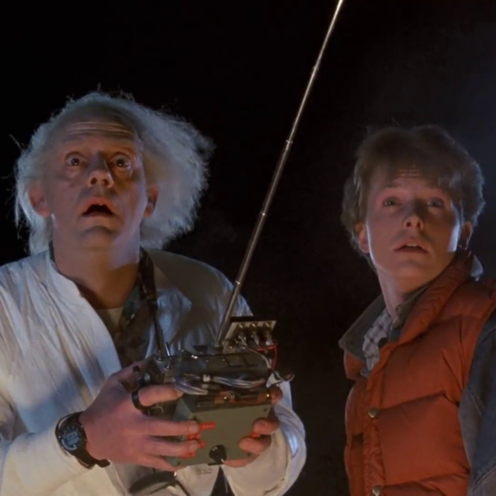 Fotograma de la película Regreso al futuro donde se va al doctor Emet Brown sosteniendo el mando a distancia con el que condujo en el tiempo por primera vez el Delorean, con su perro Einstein en su interior. Junto a él, Marty McFly