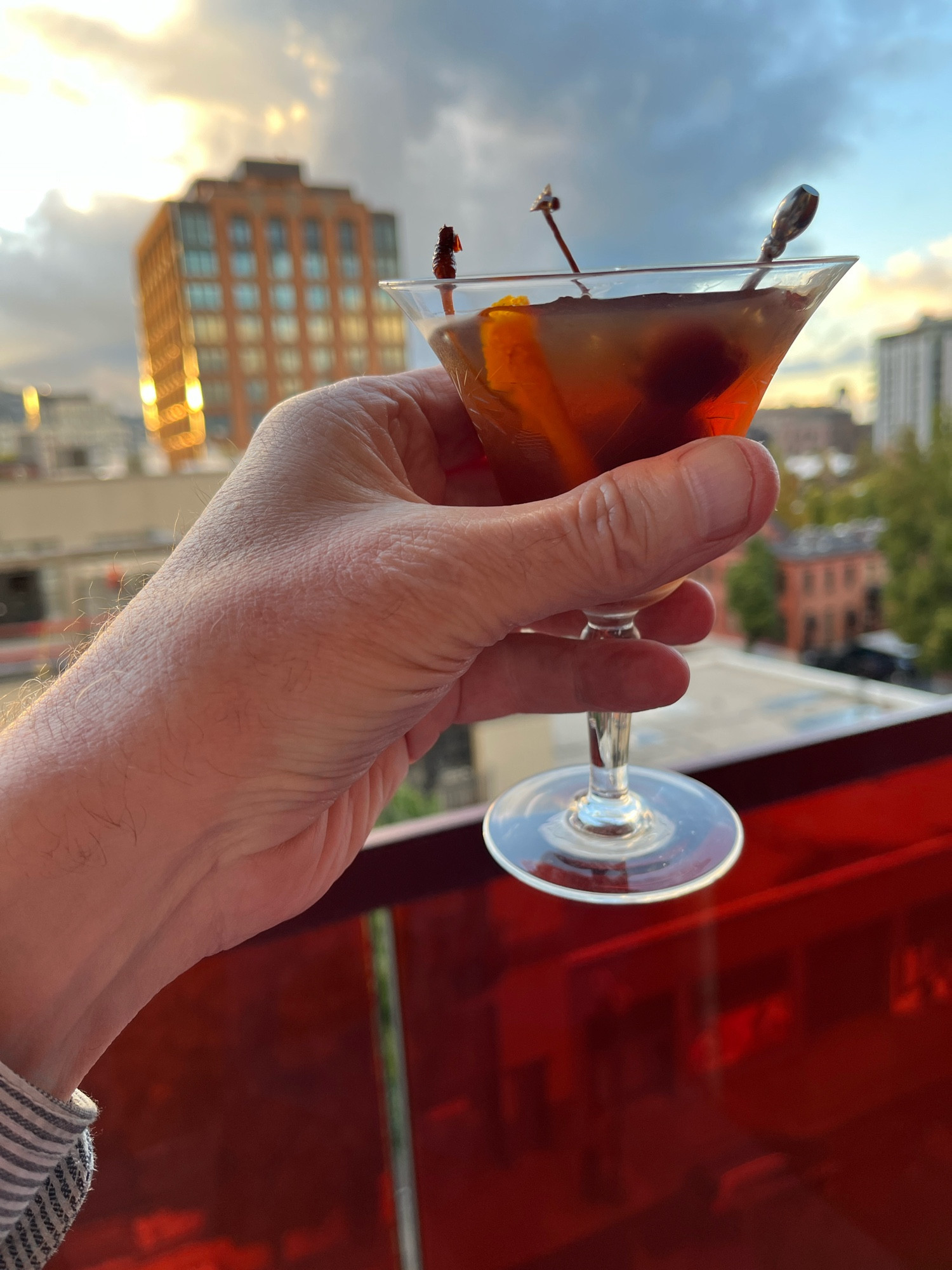 Me holding a Manhattan cocktail on the balcony looking northeast across the Pearl District on Portland, OR