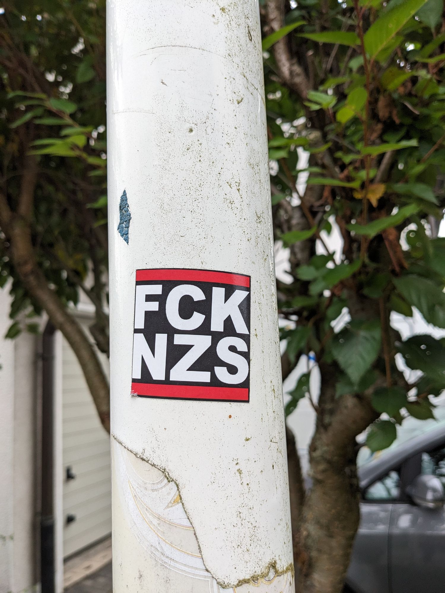 Ein Laternenpfahl mit Aufkleber 
Darauf steht 
FCK
Nzs