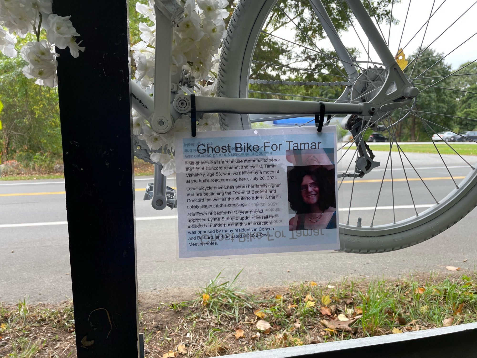 Close up of the ghost bike with the sign telling the reader of the life lost to bad design and fast driving. It also tells us that Concord and Bedford rejected the cross info even though funding would have come from the state.