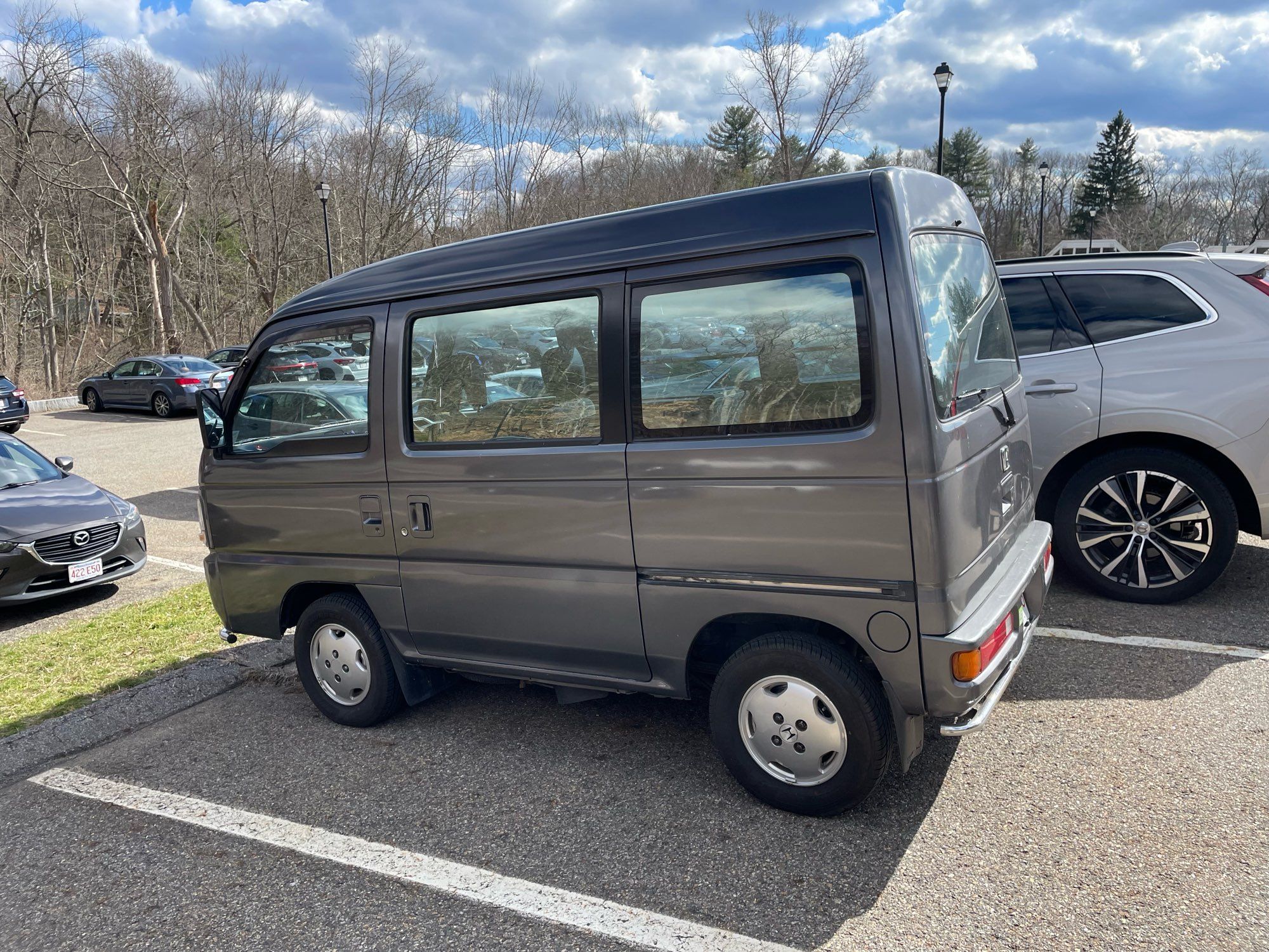 A Kei van in a parking lot. While it is a tall vehicle, it is visibly narrower and shorter than the cars around it.