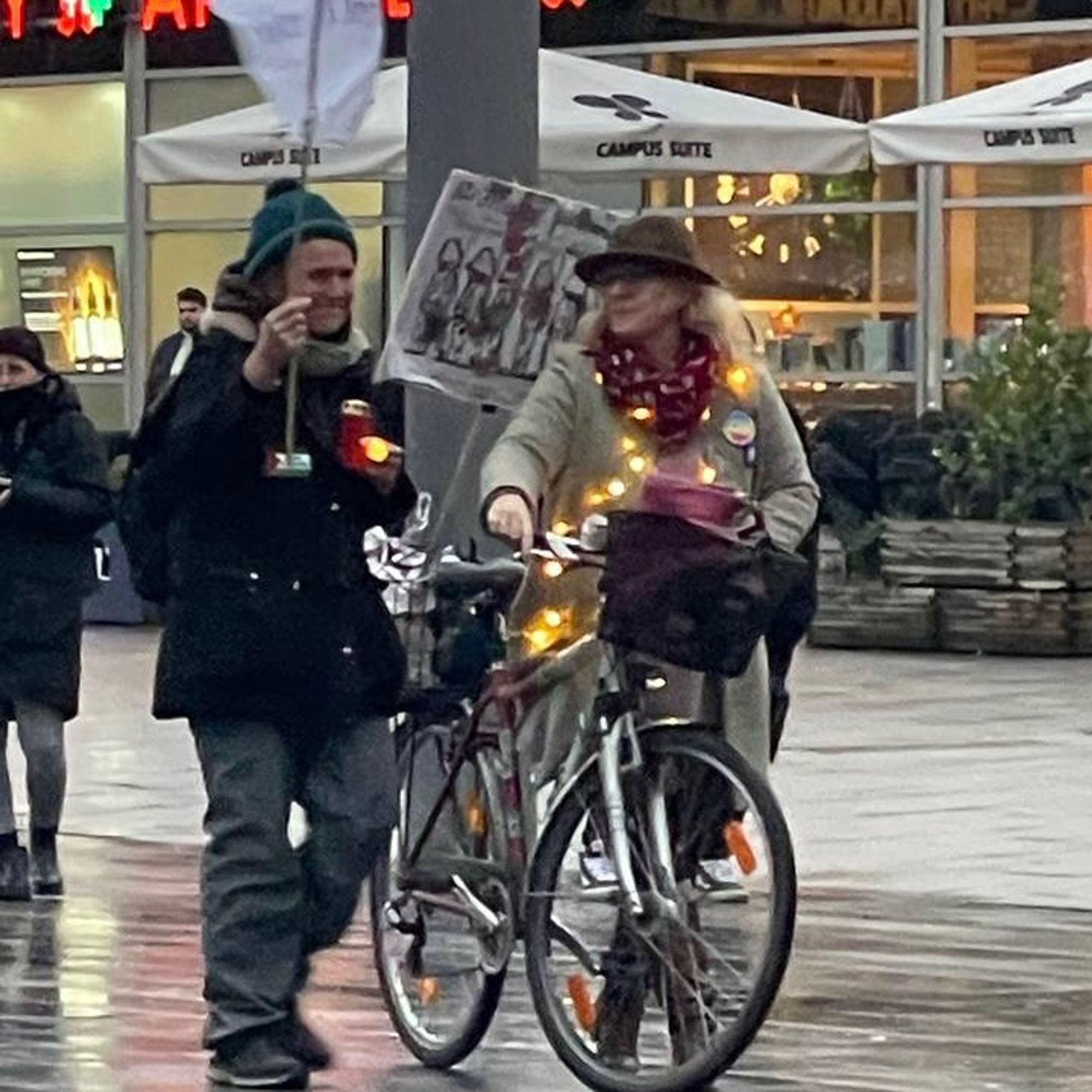 Frau mit Hut und Fahrrad hat eine Lichterkette um und plaudert mit einem Mitdemonstranten.