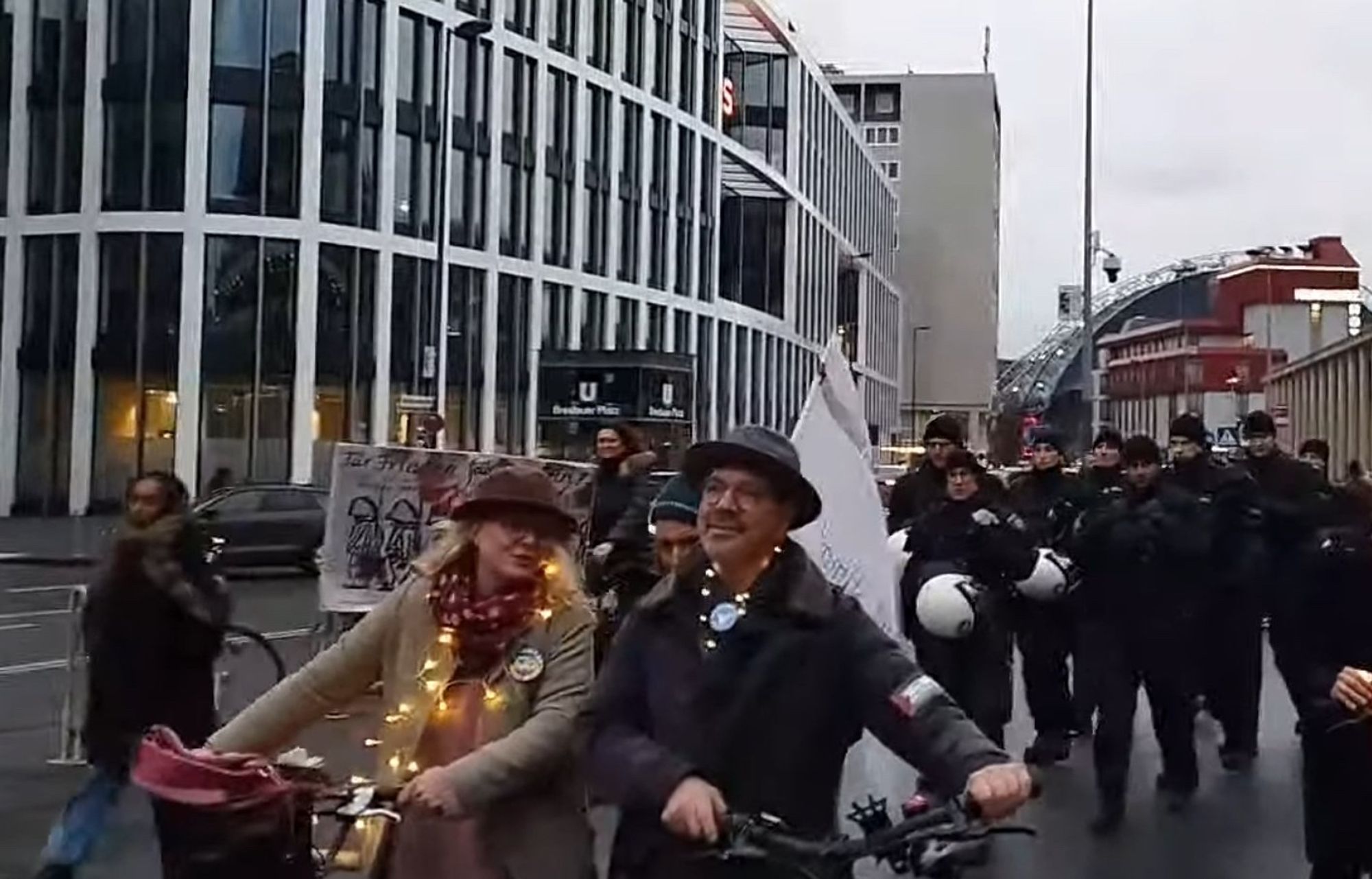 Frau und Mann mit Hut und Fahrrad auf der Demo als Lichterkette, im Rücken Polizisten