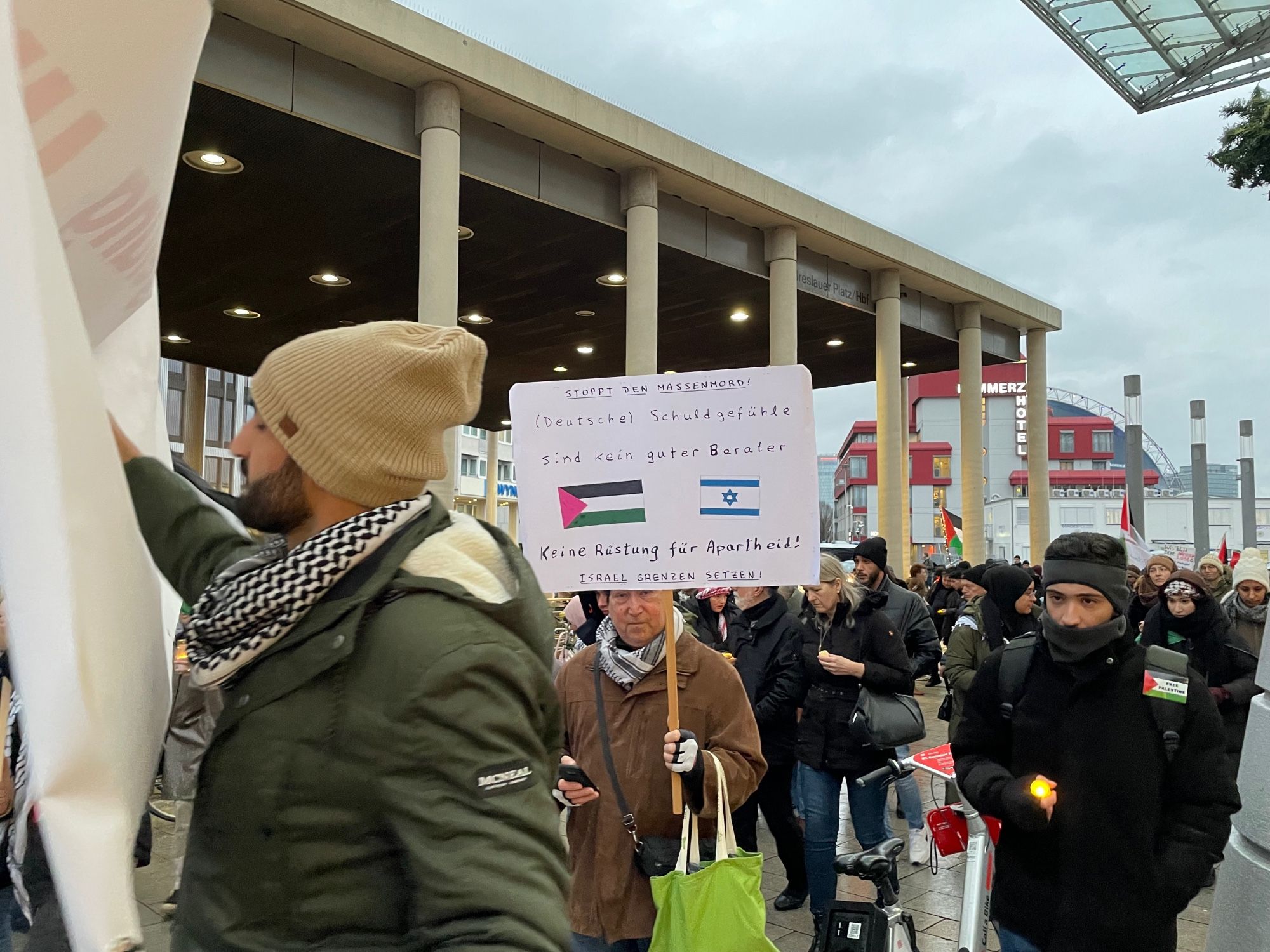 „Deutsche Schuldgefühle sind kein guter Berater“ steht auf einer Papptafel. Ein Mann in winterlicher Kleidung präsentiert sie am Breslauer Platz am Hbf köln inmitten der Gaza-Hamas-Demo.