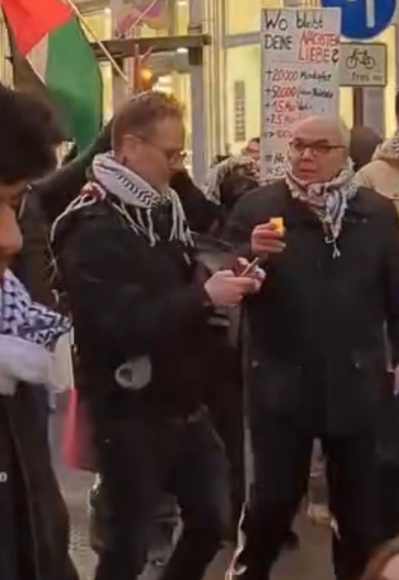 Zwei Männer im Palituch mit Kerze in der Hand marschietrn auf Demo durch köln. Sie haben winterliche Kleidung an.