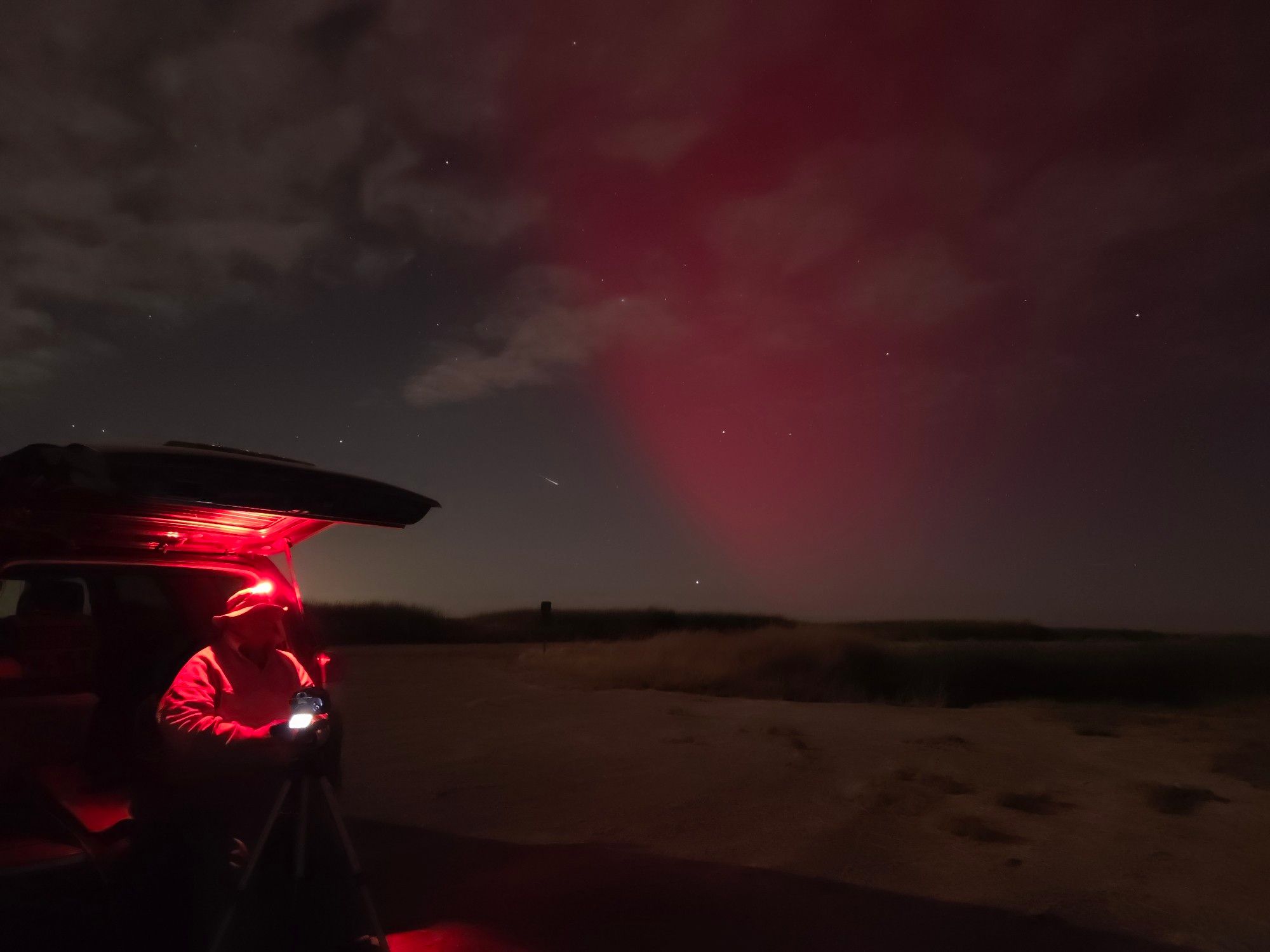 The red aurora lights up a small portion of the star filled sky, while trekrr sits in the back of the 4Runner, his red headlamp causing the space around him to glow red. The desert landscape is lit by the pale white moonlight.