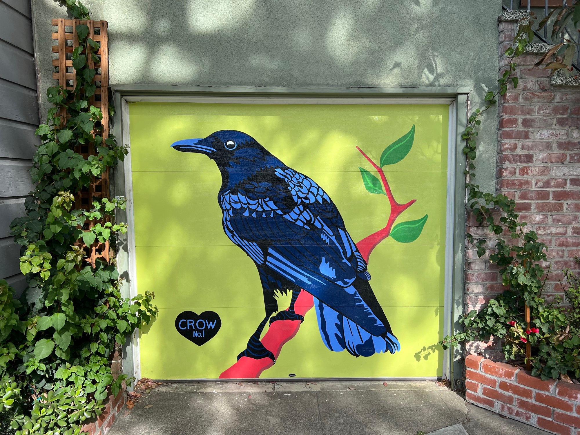 Garage door mural of a black and blue crow sitting on a red branch with green leaves. The background is lime green. There is a black heart next the crow. It says Crow no. 1