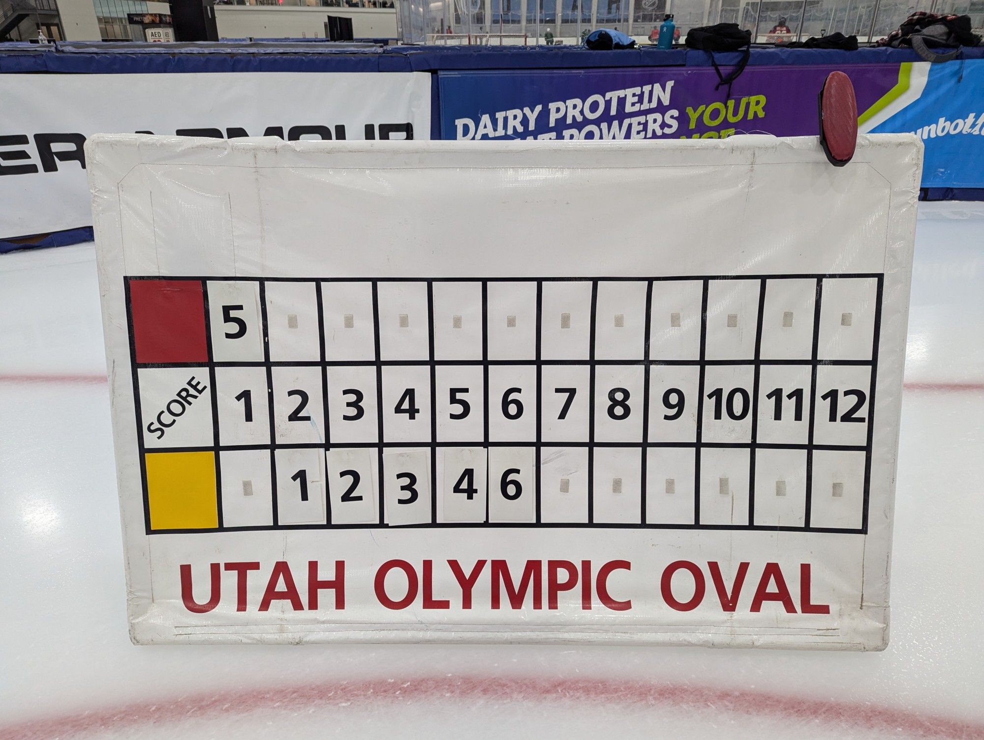 An analog scoreboard is positioned on an ice rink at the Utah Olympic Oval. The final score is 6 yellow vs. 1 red.