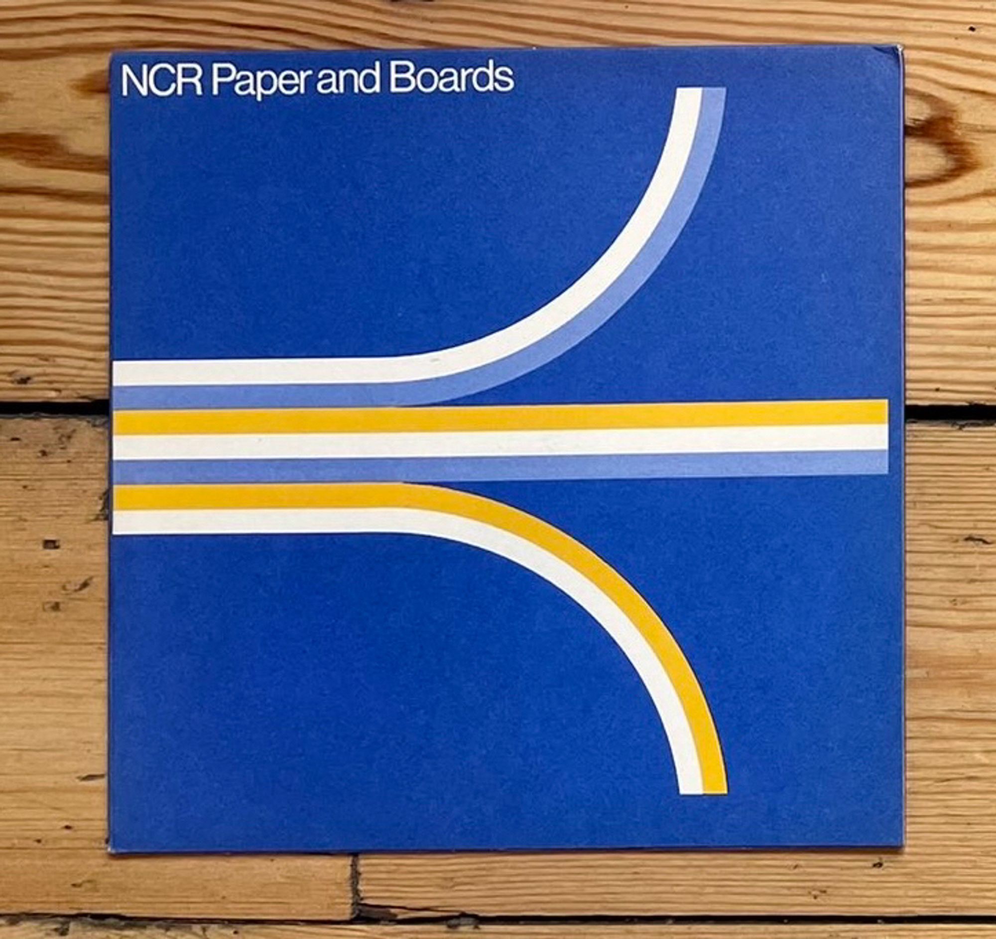 NCR Paper and Boards sample book by Wiggins Teape (Merchants) Ltd. According to its owner (print collector Matt Lamont, of Design Reviewed) it dates to the 1960s.

It’s a square royal blue book with three stylized white/yellow/light blue lines that look remarkably like the well-known Atari “Fuji” logo, purportedly designed in the early 1970s. It reads “NCR Paper and Boards” in the upper left.