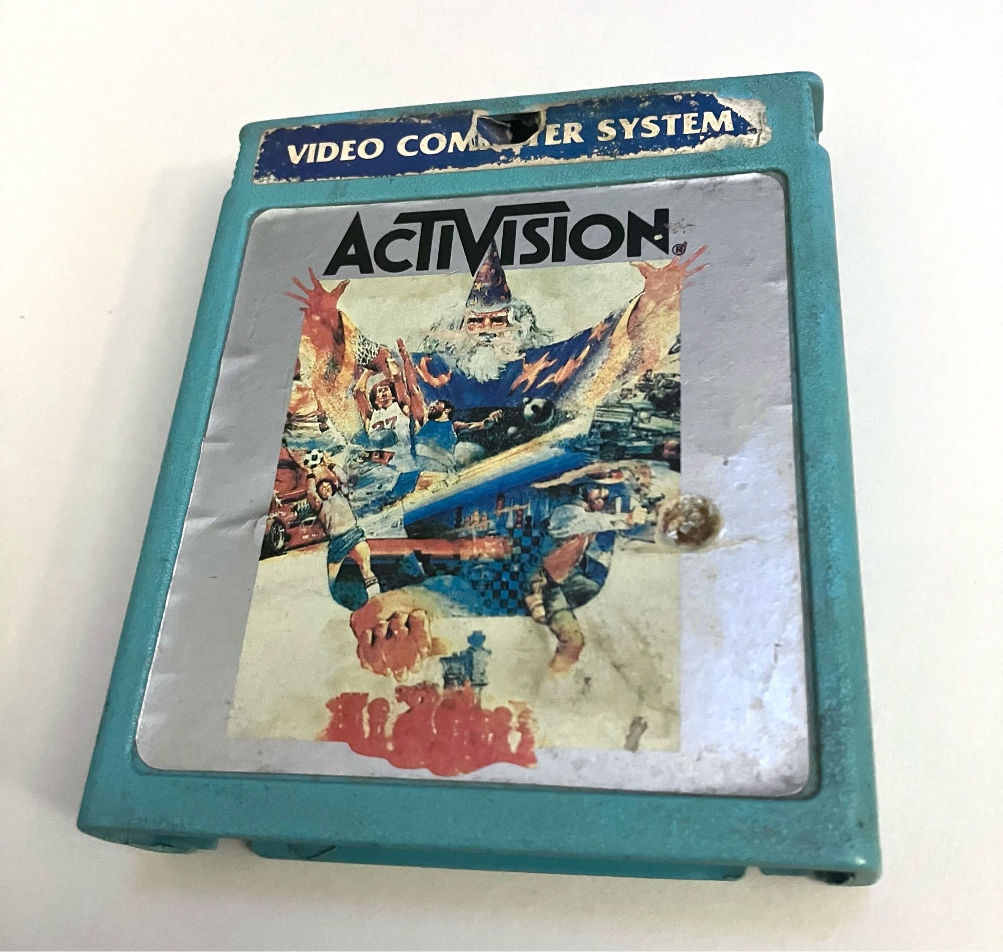 A light blue 2600 cartridge featuring a silver color label with ActiVision in black text above collage artwork featuring the wizard from Atari’s “Brain Games”, among other Atari game related art.