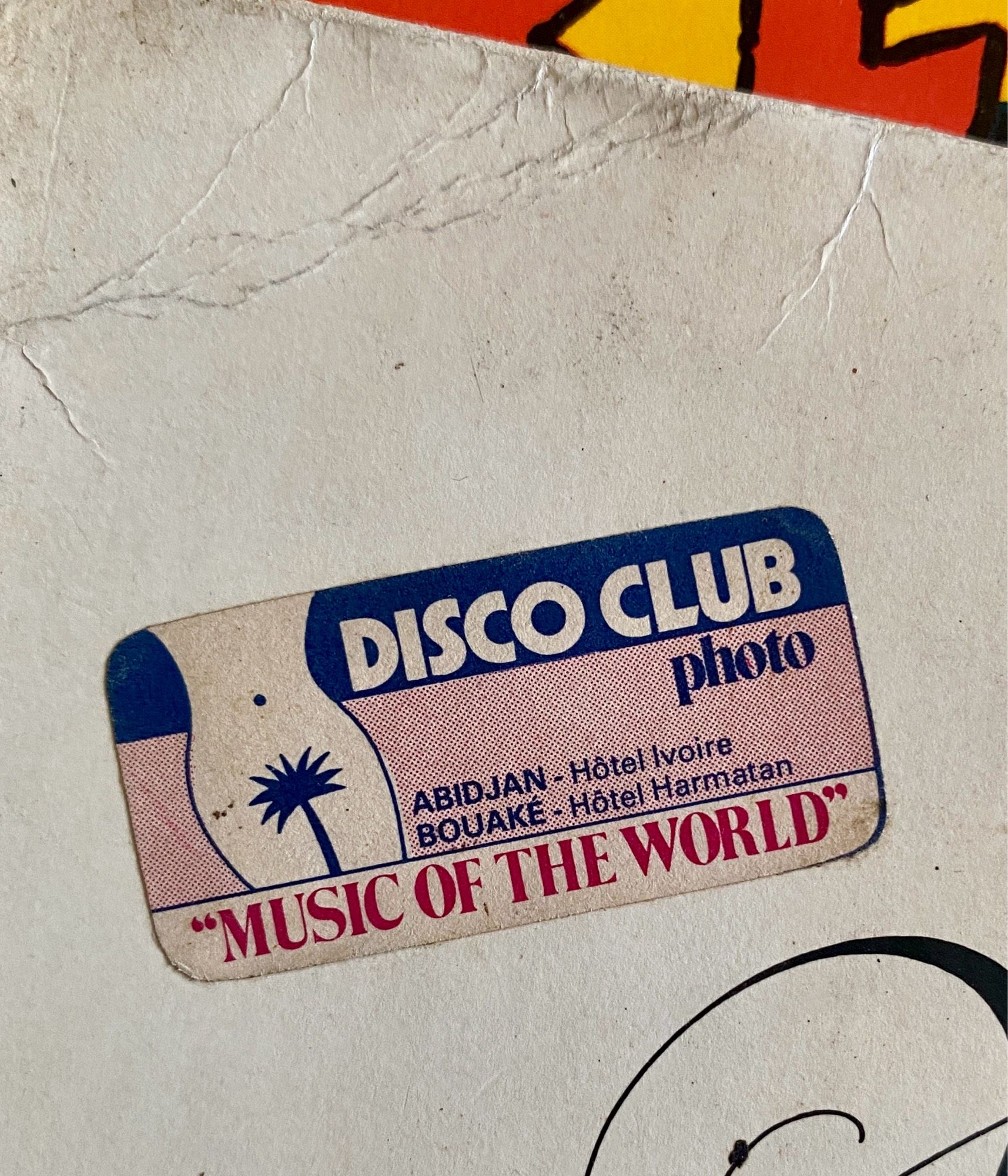 Étiquette collée sur la pochette d’un vinyle d’occasion (Sarah Vaughan Songs of the Beatles) qui représente un palmier stylisé qui forme le pubis d’une femme avec écrit autour: 
Disco club photo
Abidjan- Hotel Ivoire
Bouaké- Hotel Harmatan
« Music of the World »