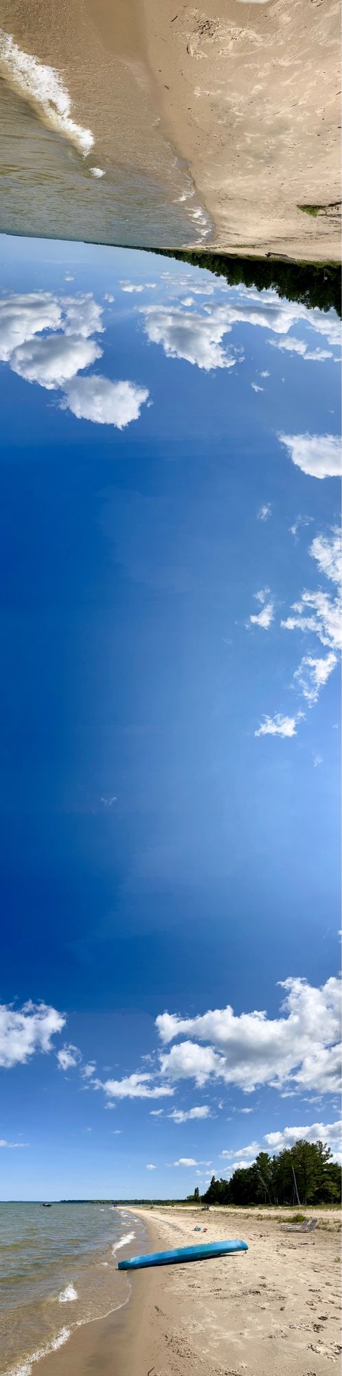 overturned blue kayak on a beach under fluffy clouds and an azure sky