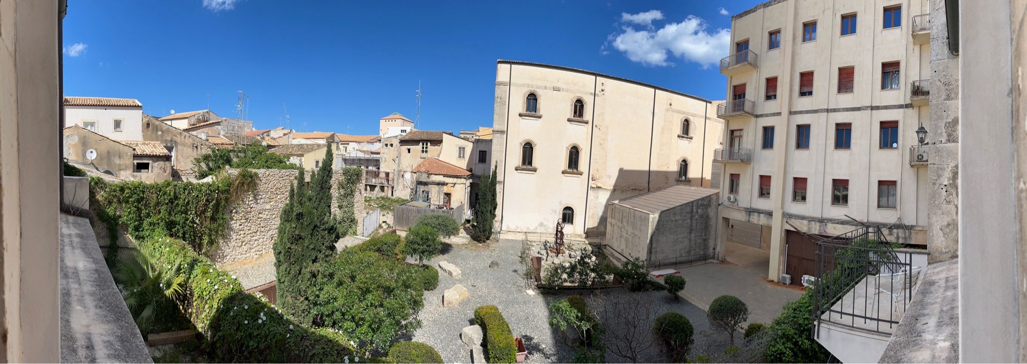 large courtyard with stone and brick buildings under terra cotta tiles under a blue sky with a couple small white clouds