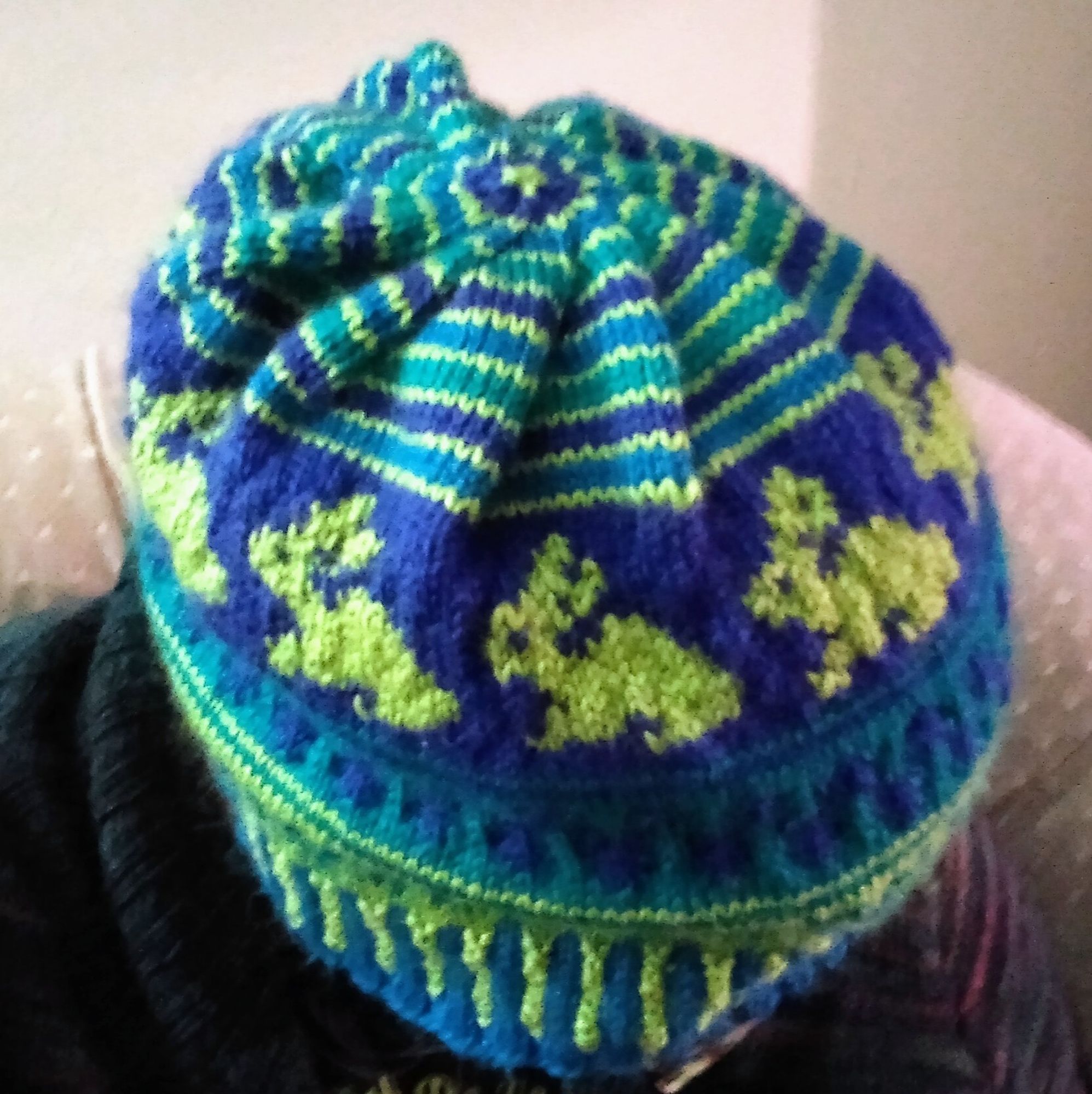 A knit hat with a bunch of detailed colour designs. From the top down:
- a series of concentric stripes in royal blue, teal, and aqua blue, with each stripe separated by a thin line of neon green.
- neon green bunnies on royal blue
- aqua blue dots on teal
- a teal X and + design on neon green, and
- a vertical ribbed edge with neon green and aqua blue alternating stripes