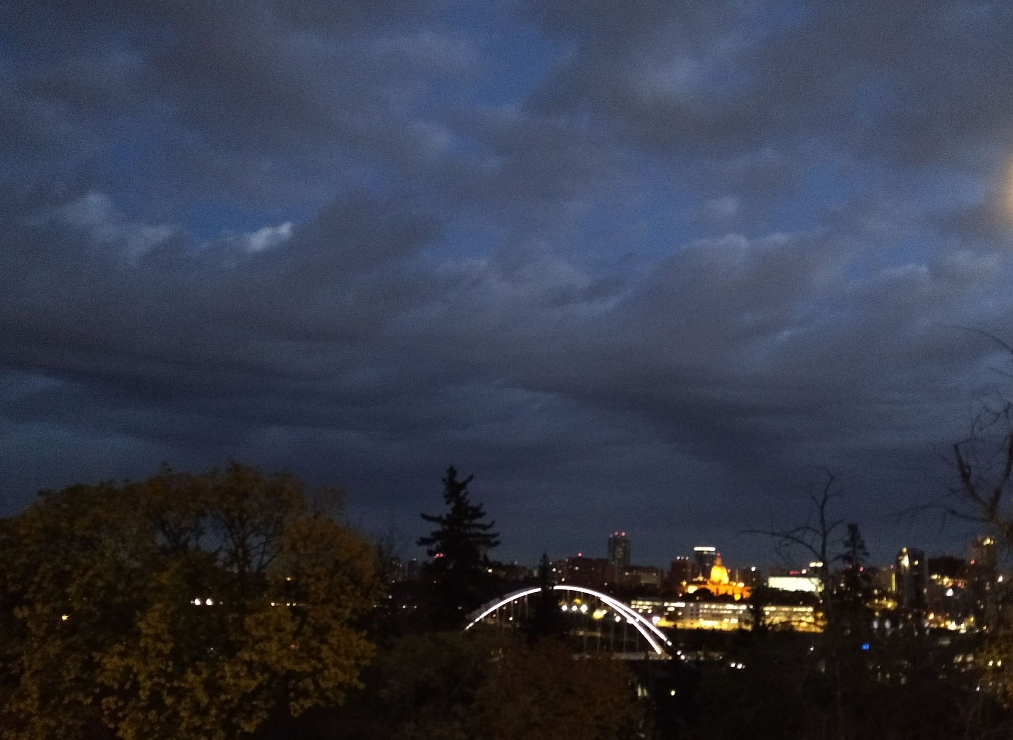 A less-obscured view of the Legislature as the cupola glows brightly orange and the Walterdale bridge arcs in white out of the river valley's depths.
More lights brighten additional government buildings behind the bridge and below the legislature.