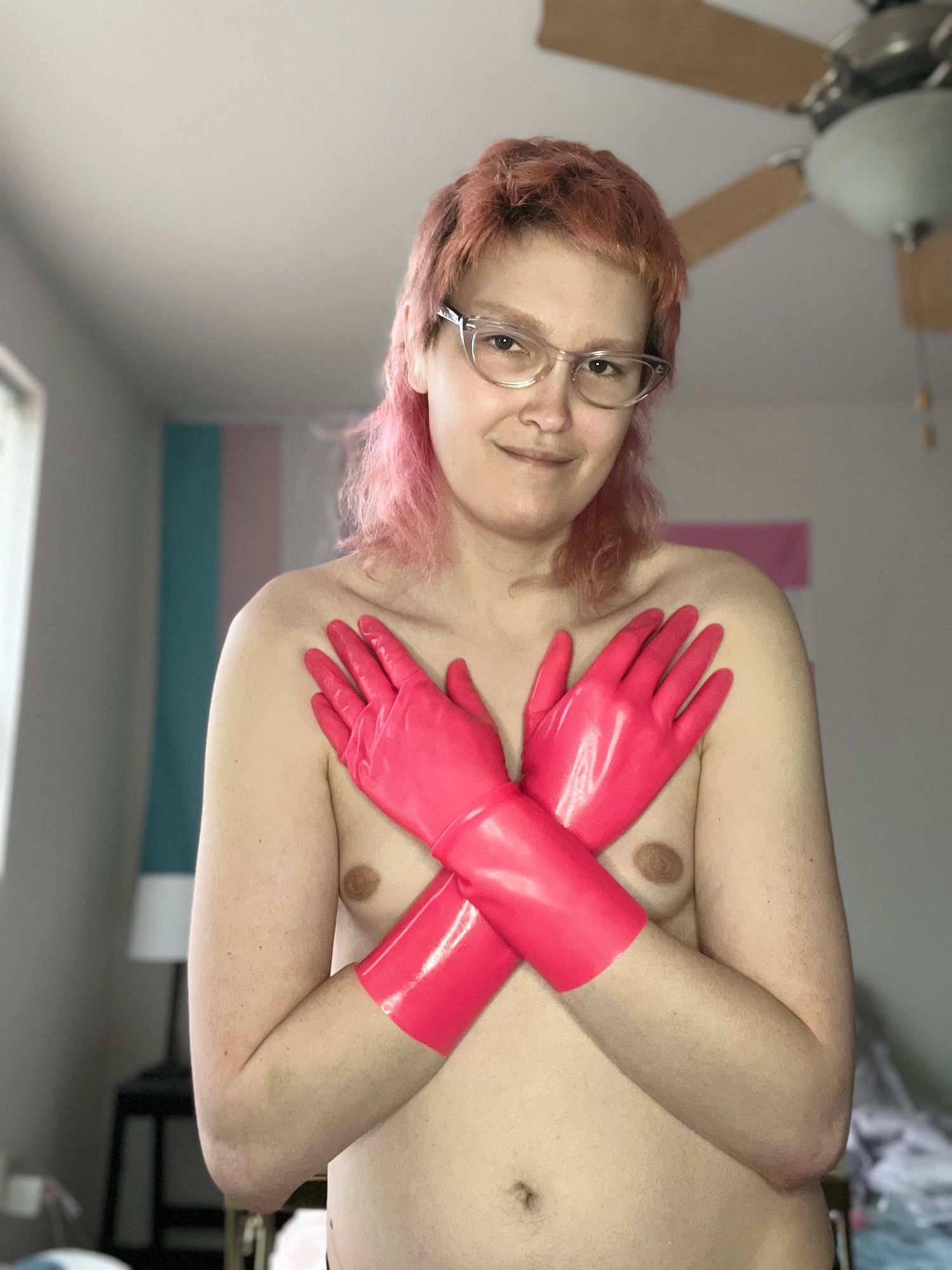 Pink mullet trans girl naked. Upper torso visible. Arms crossed across the chest wearing pink latex gloves
