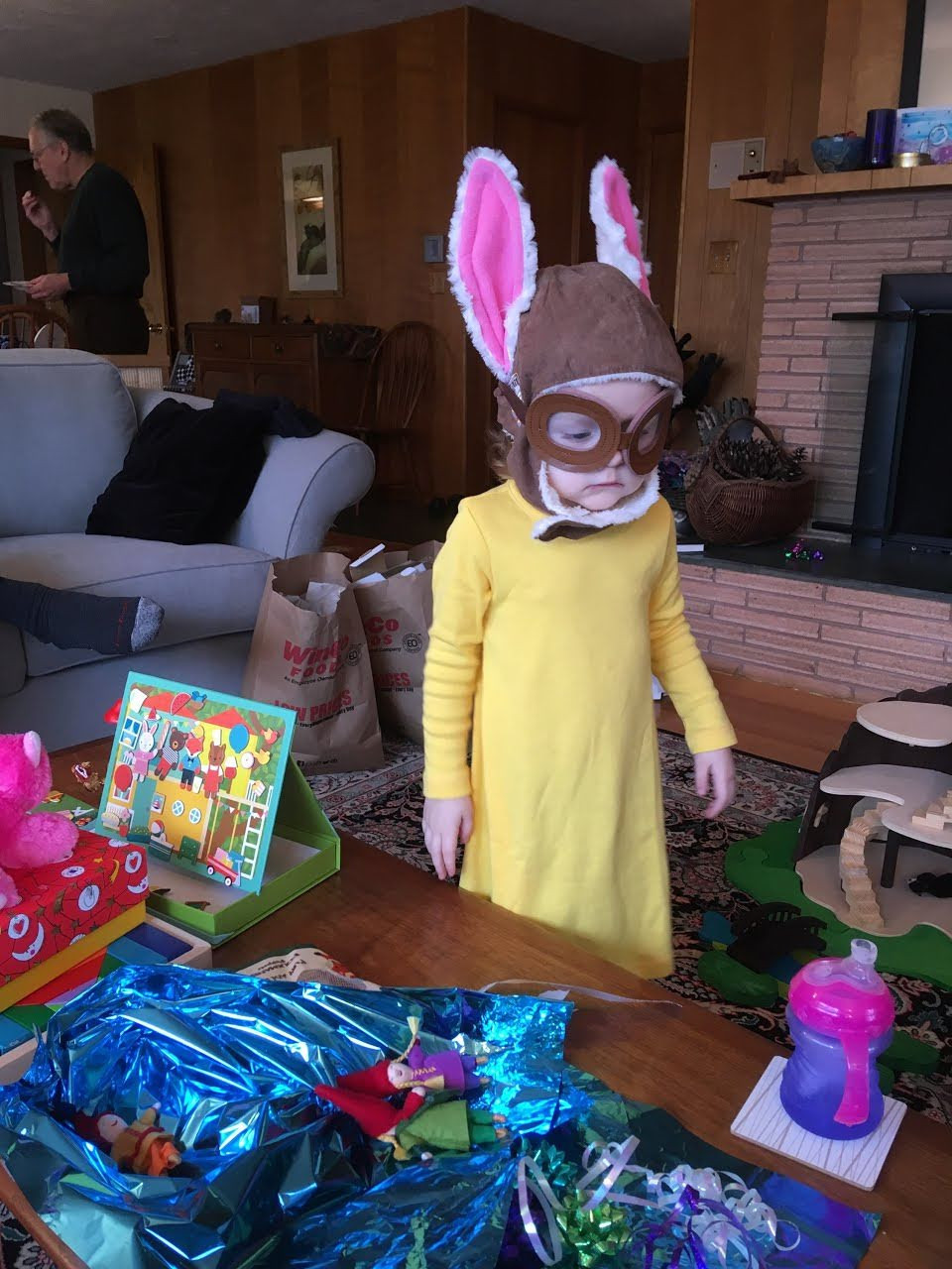 A three year old child wearing an aviation helmet, goggles, and rabbit ears.