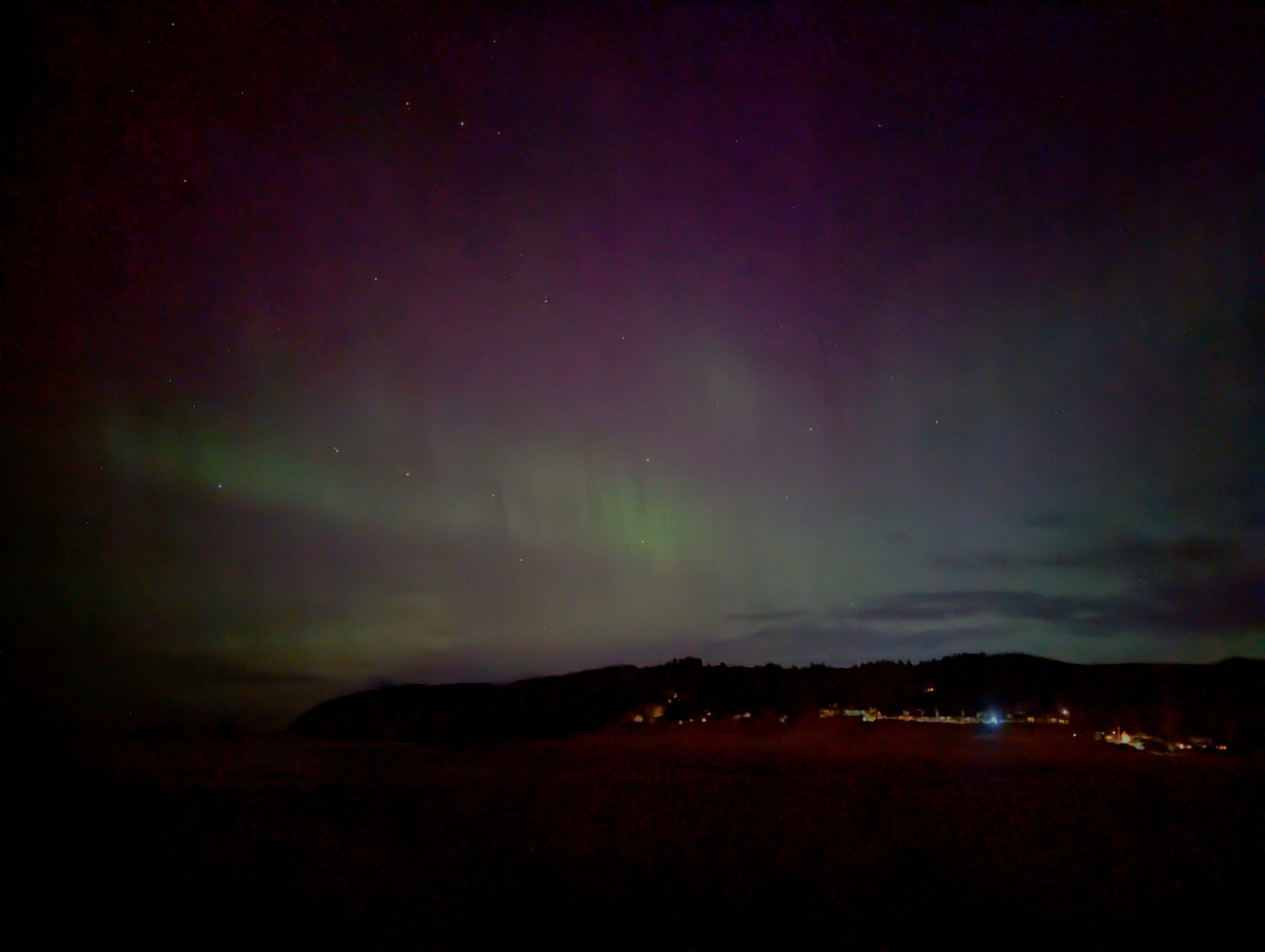 Green curtains and pink haze of aurora over black beach hills.