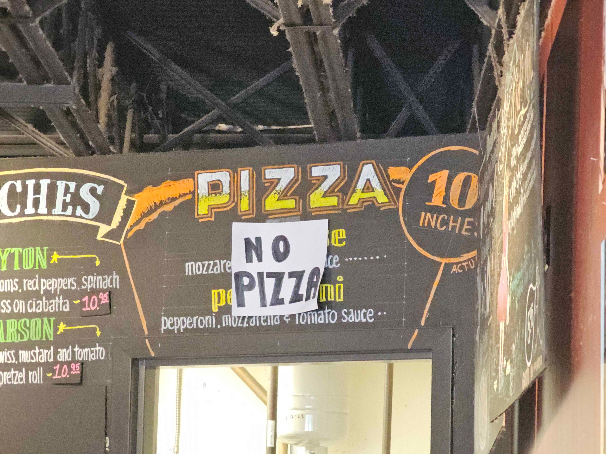 A sign advertising pizza covered by another sign that's says no pizza.