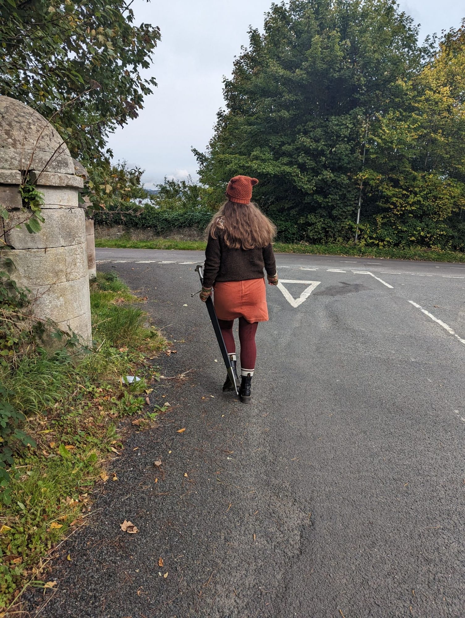 A photo of me from behind as I was down a street holding my sword, Andúril. I'm wearing an autumnal outfit of orange, brown, and burgundy.