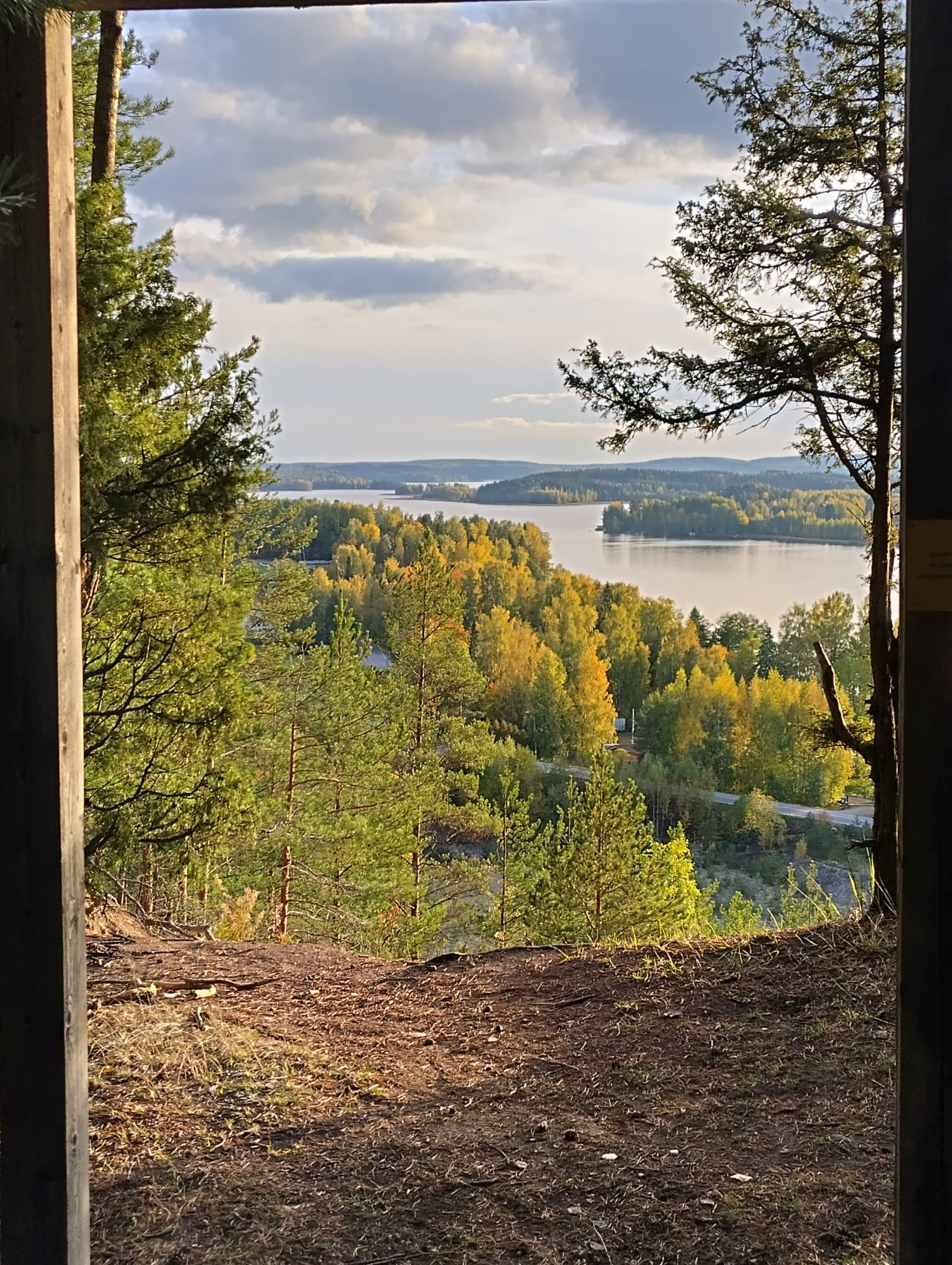 A view from a hill through a wooden gateway to a scenery of autumn forests and lakes