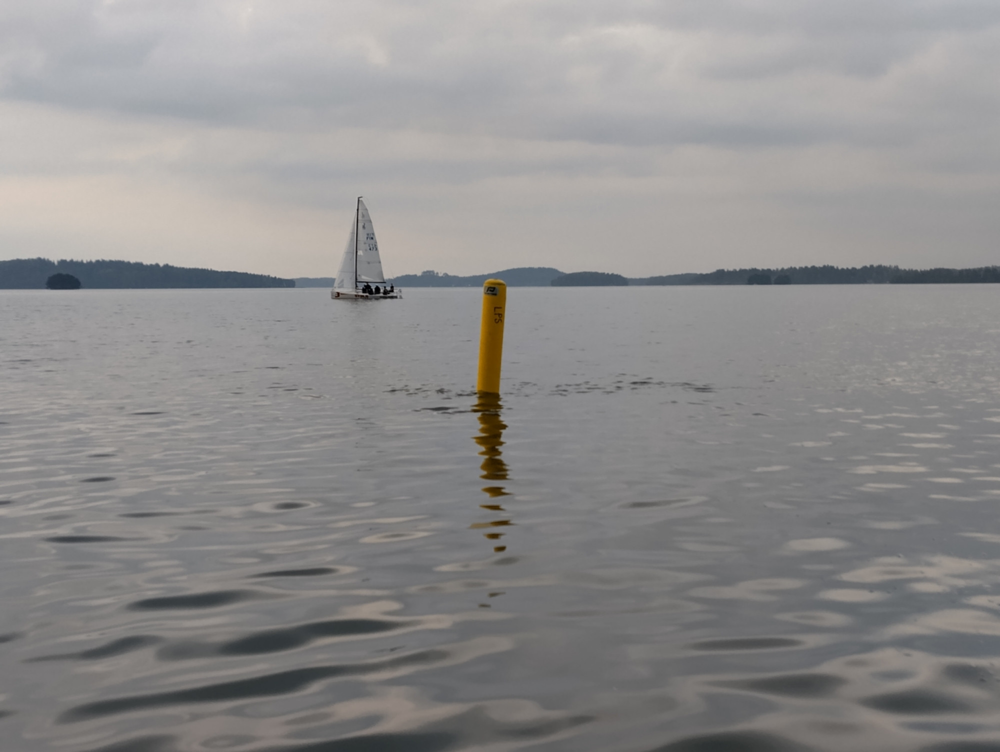 A small racing yacht on a lake behind a yellow buoy