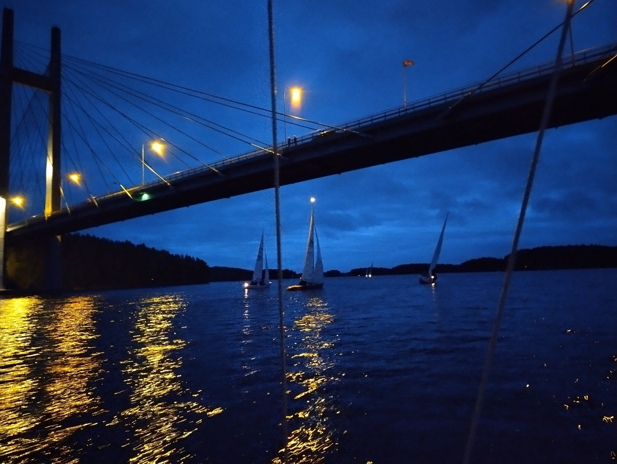 3 sailing boats passing under a bridge at night