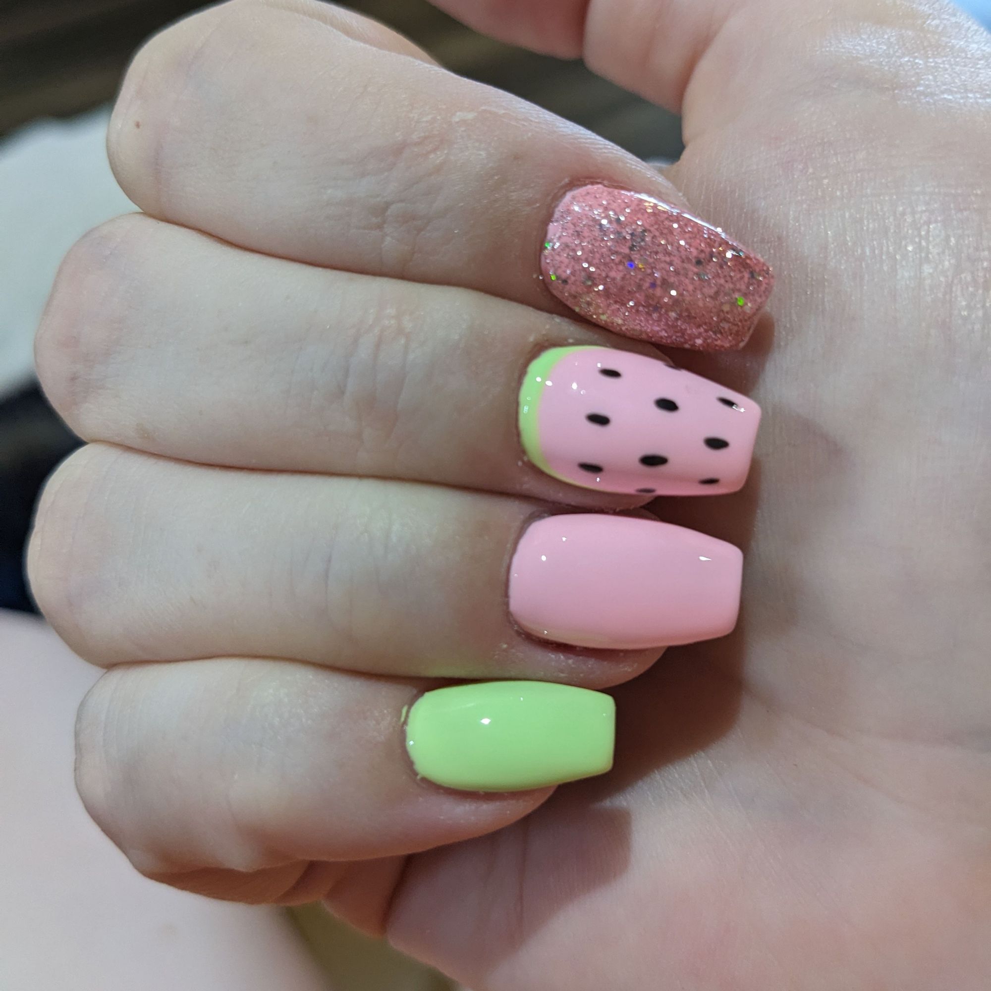 Manicure of pastel colors. Green pinky nail, pink ring finger, watermelon design on middle, pink sparkles on index.