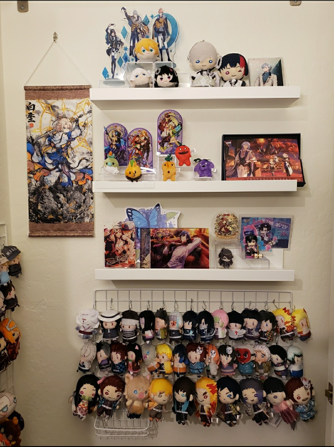 Wall with 3 shelves of acrylic standees and other misc from multiple fandoms, a rectangle grid holding a collection of Demon Slayer finger puppets/nito-tan, and a fanart wallscroll of Xianxia Albedo from Genshin Impact.